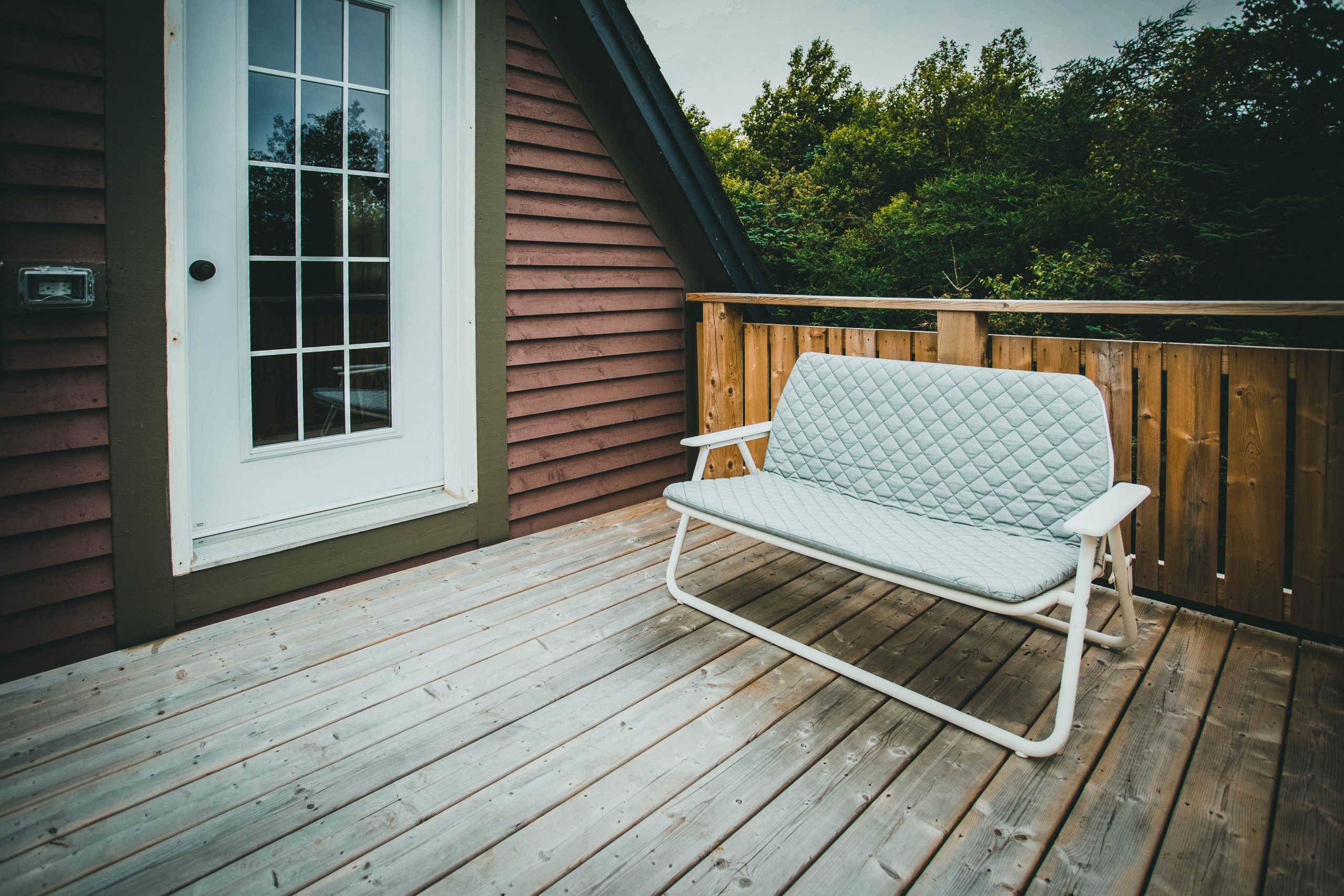 A peaceful outdoor deck scene with a cushioned bench and wooden railing amidst trees.