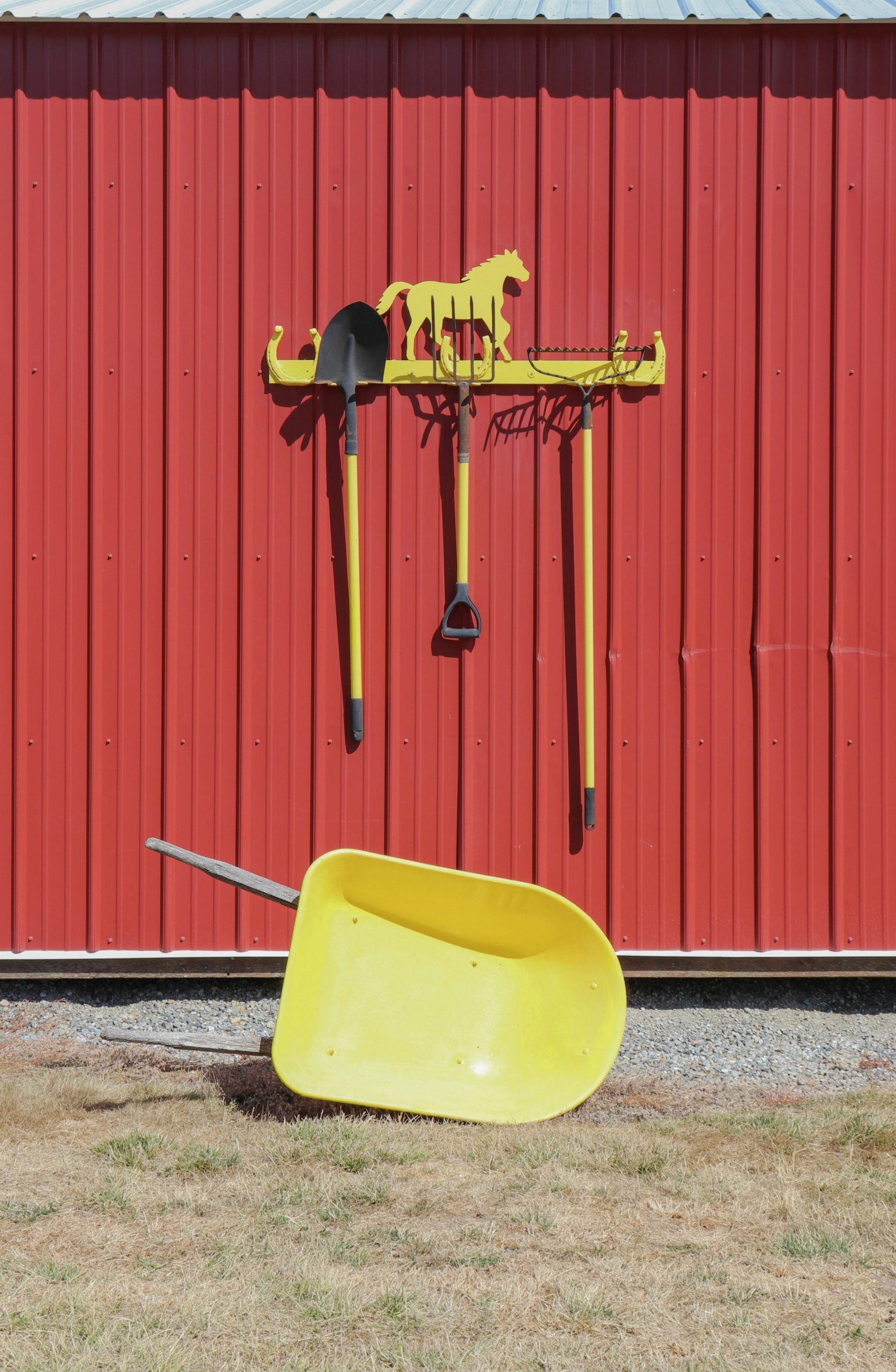 A selection of yellow ranch tools o a red barn.