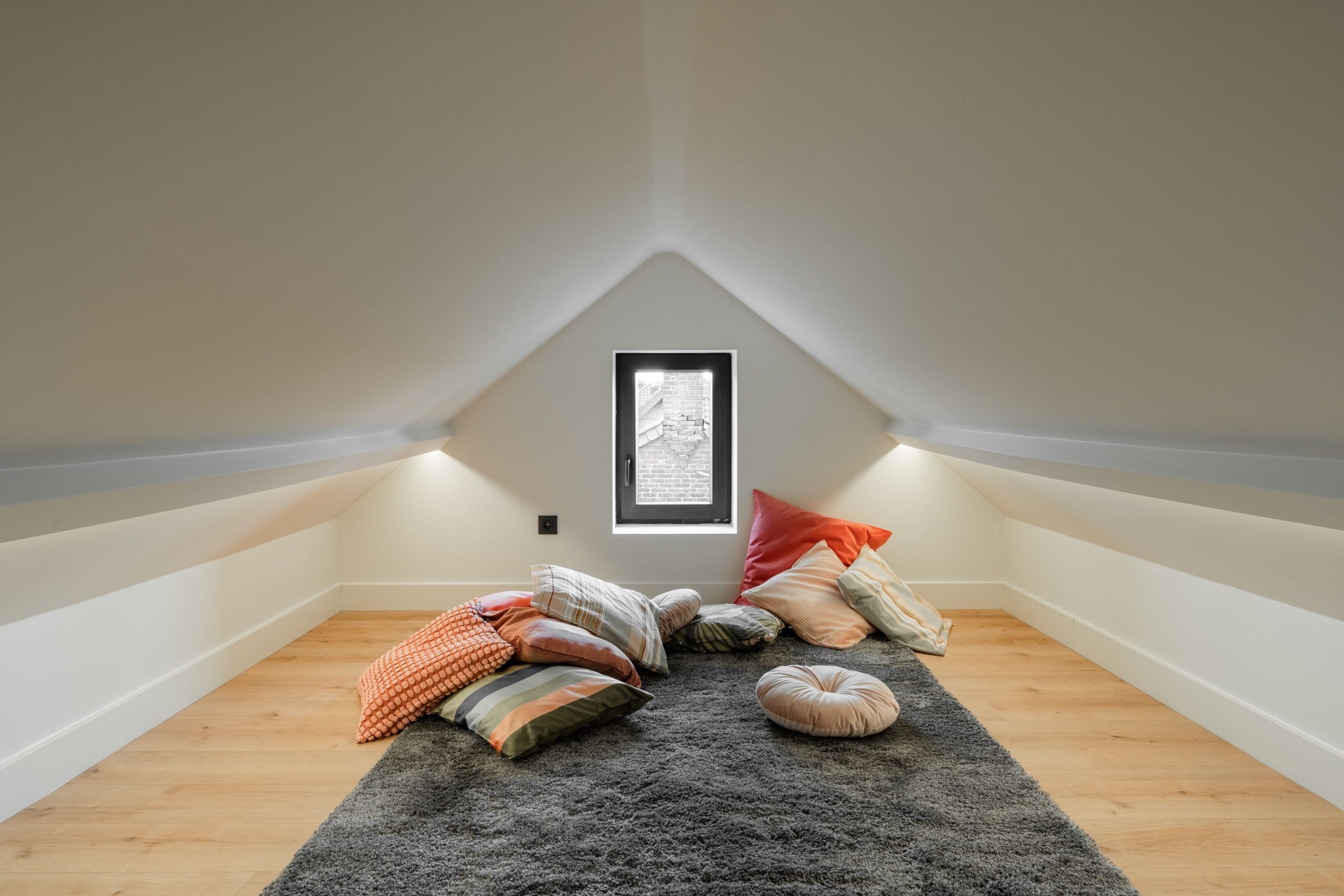 A serene attic room featuring colorful pillows and soft lighting, perfect for relaxation.