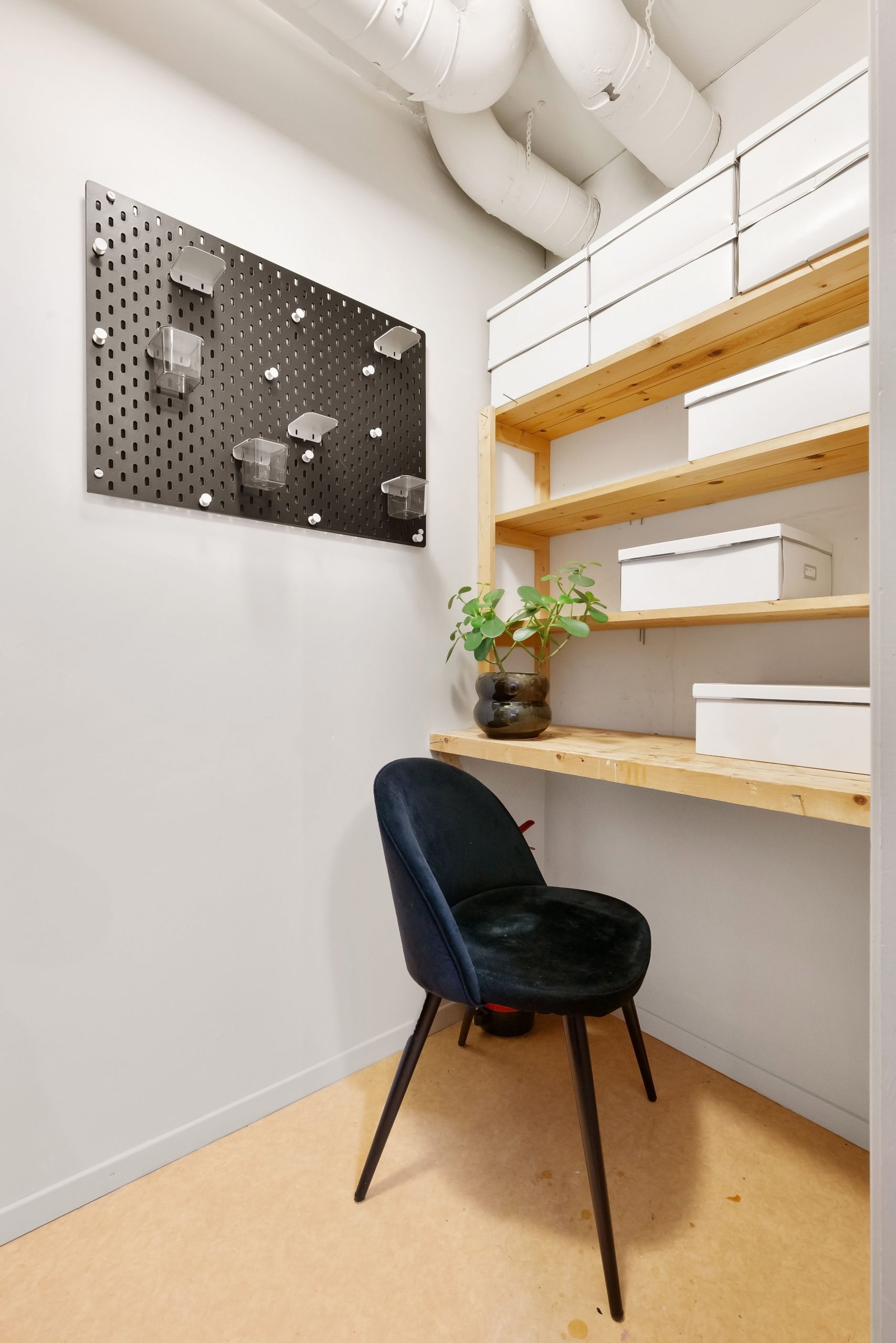 A sleek, minimalist home office with black chair, shelves, and pegboard for organization.