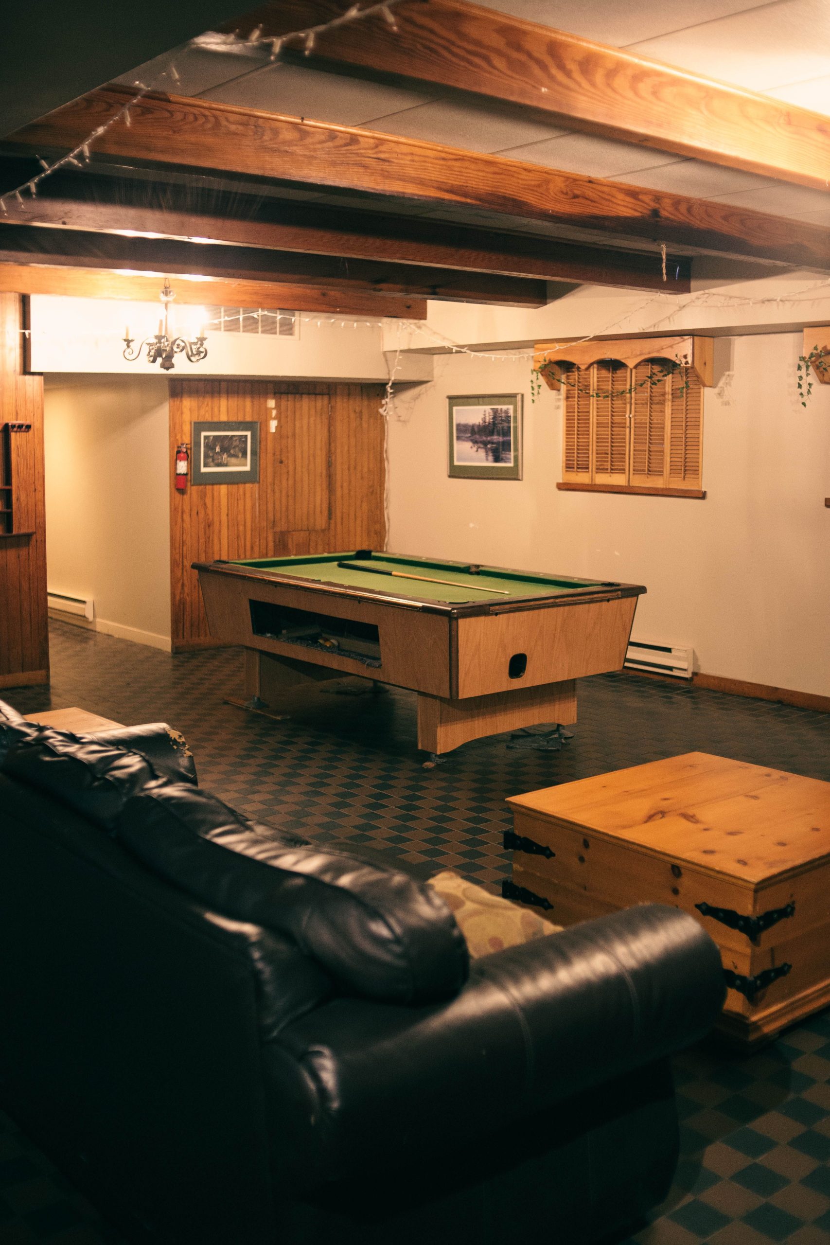 A warm and inviting basement game room featuring a pool table, couch, and wooden decor.