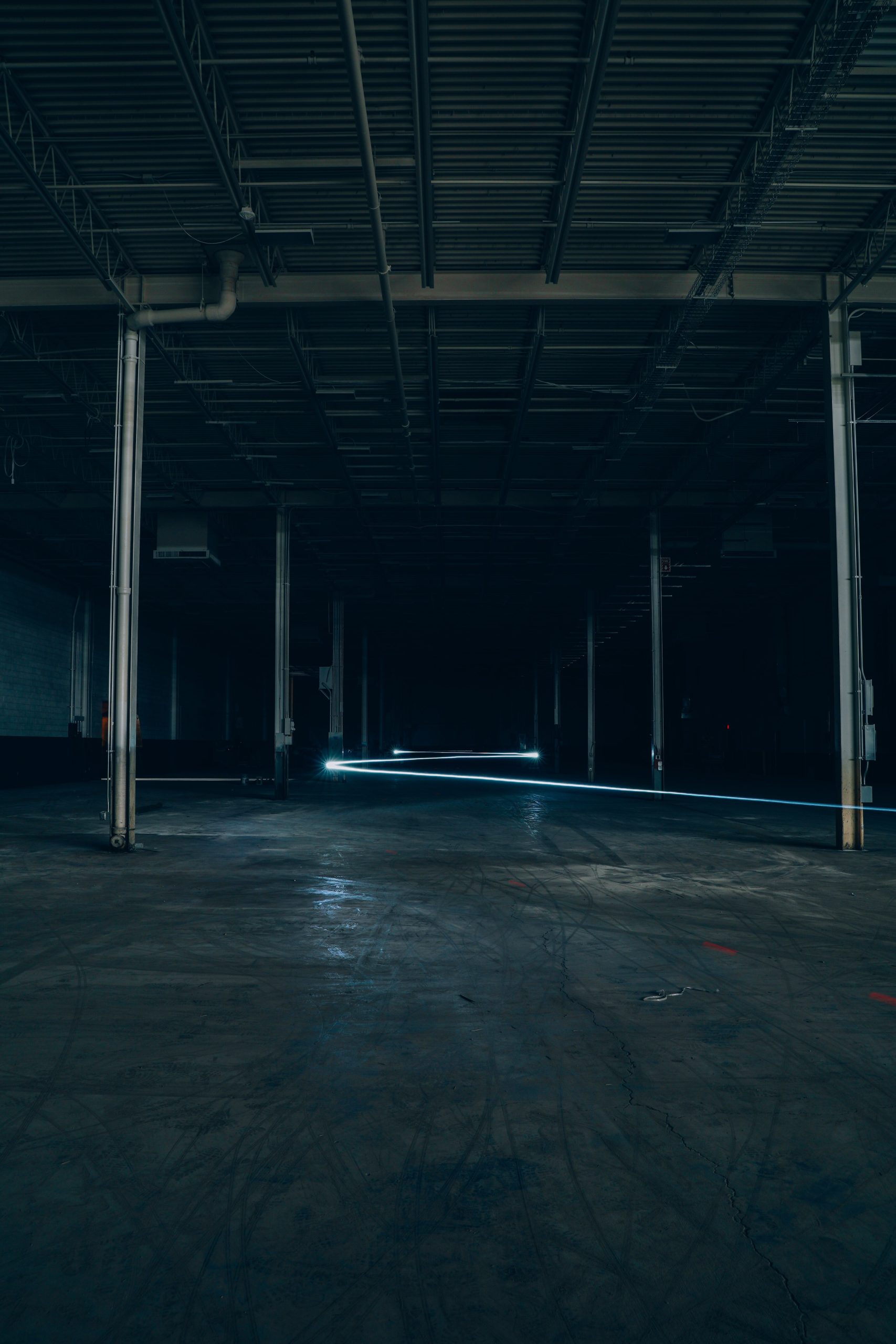 An empty, dark warehouse with visible steel columns and a concrete floor, perfect for industrial shoots.