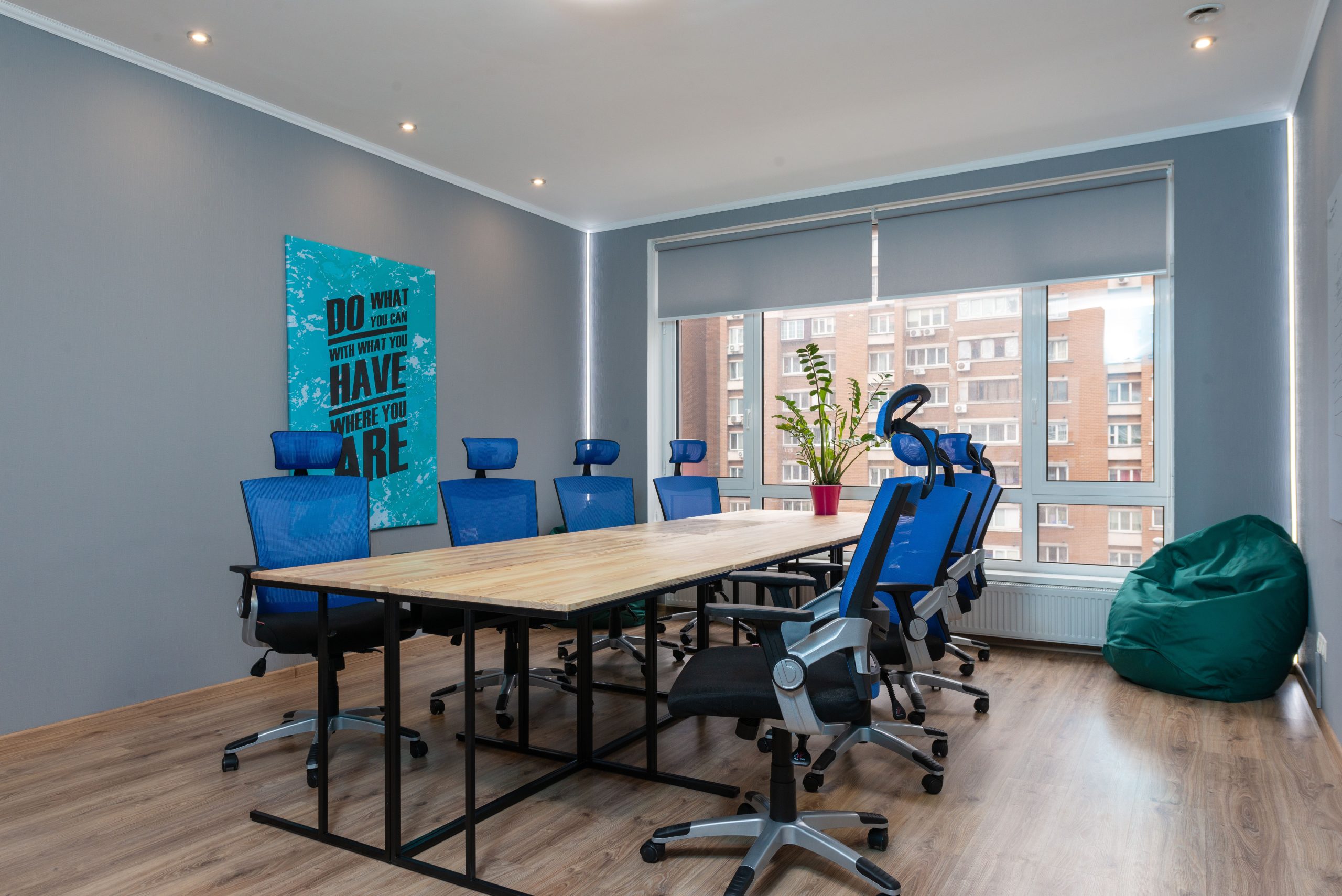 Blue armchairs at wooden table placed in modern conference room with decorative signboard with inscription and window in stylish office building