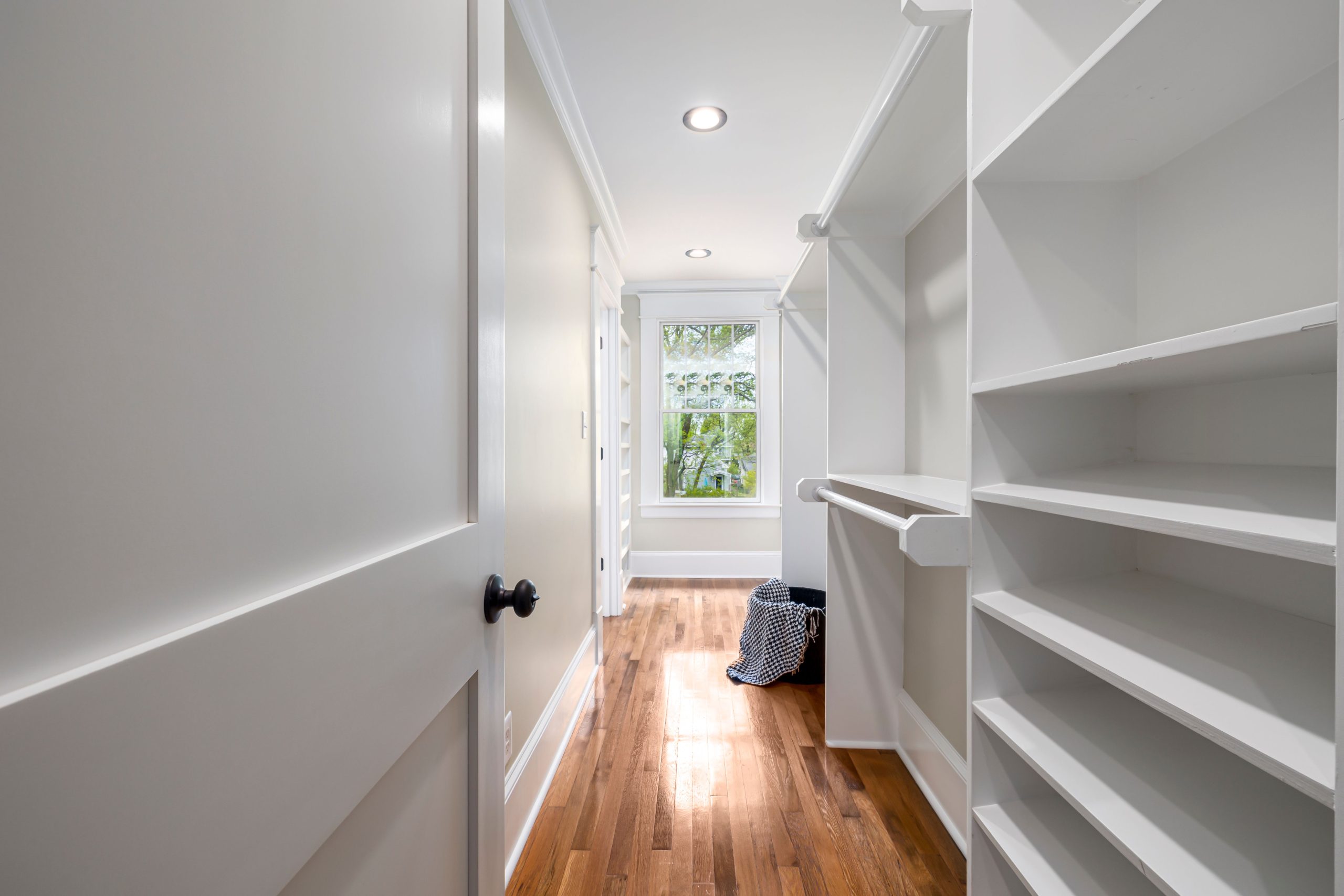 Bright, modern walk-in closet featuring white shelves and wooden flooring. Ideal for home interiors.