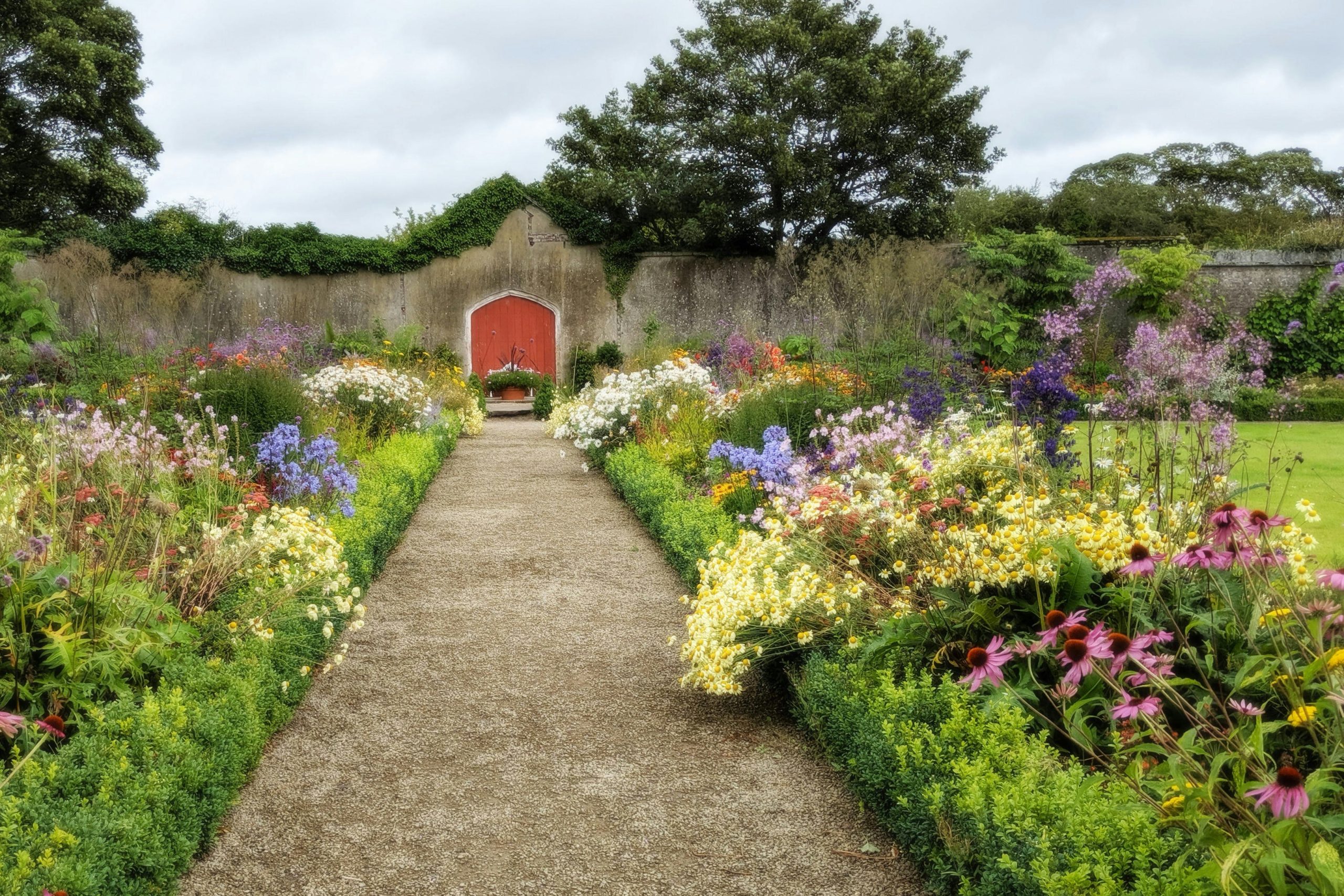 Colorful flower borders line a gravel path through the walled garden at Duckett's Grove castle.