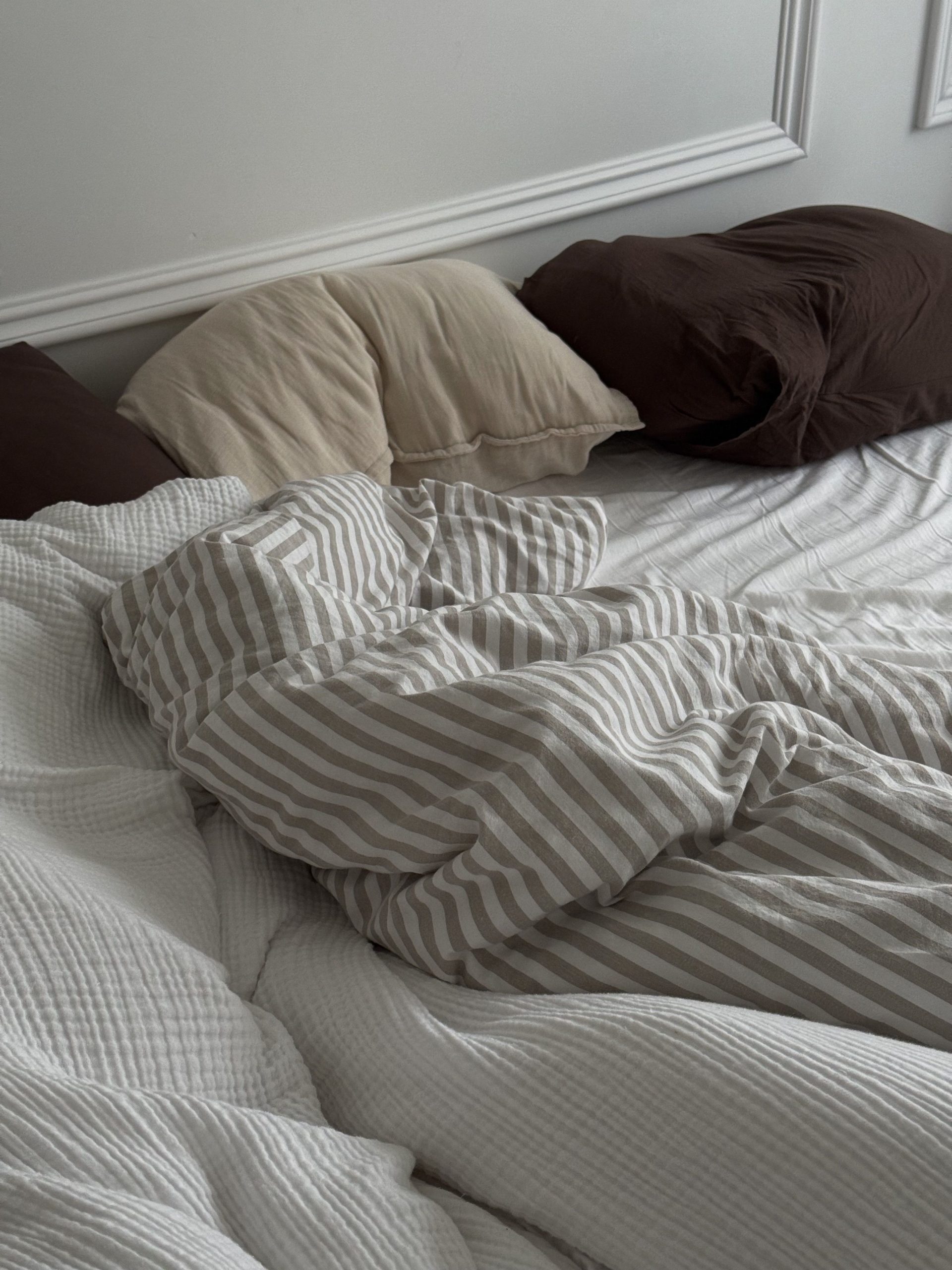 Comfortable unmade bed with striped bedding and pillows, ideal for interiors or lifestyle themes.