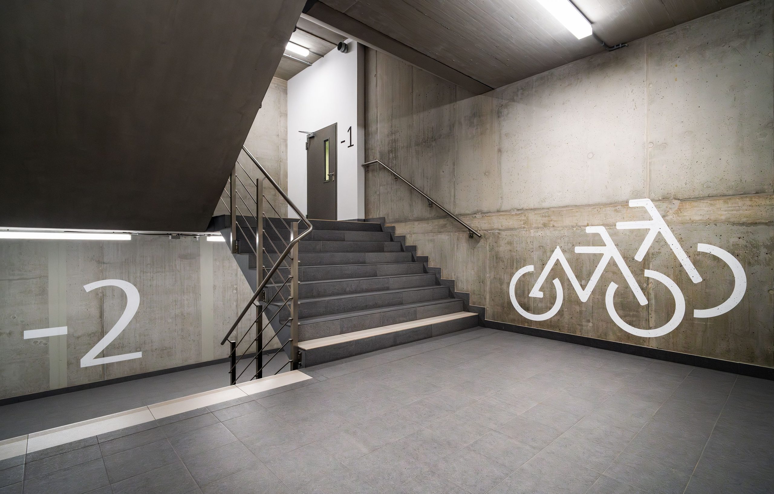 Explore a modern concrete stairway leading to underground bicycle parking, with industrial railings in Poznań.