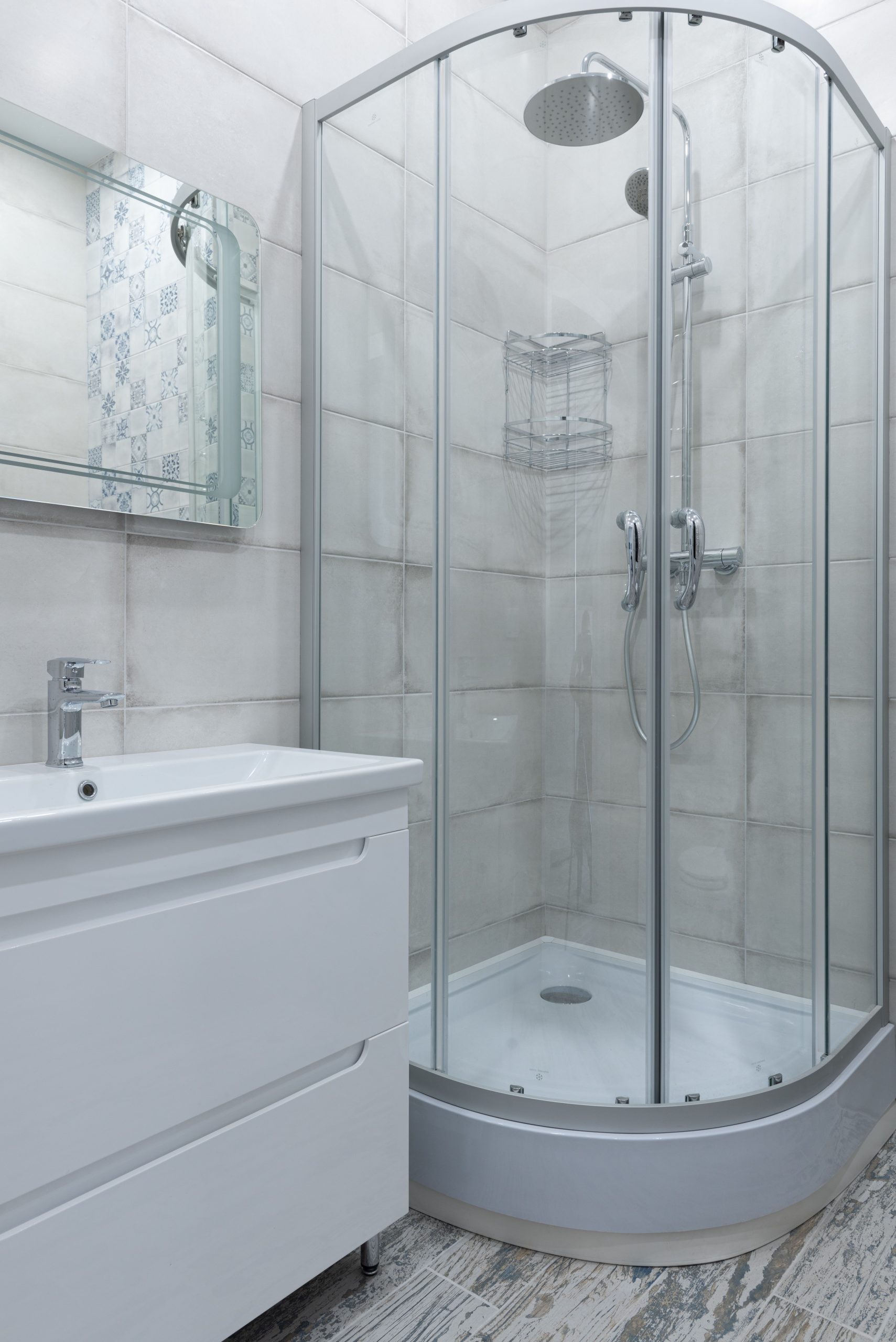 Interior of modern light bathroom with glass shower cabin placed at corner near sink and mirror on wall at home