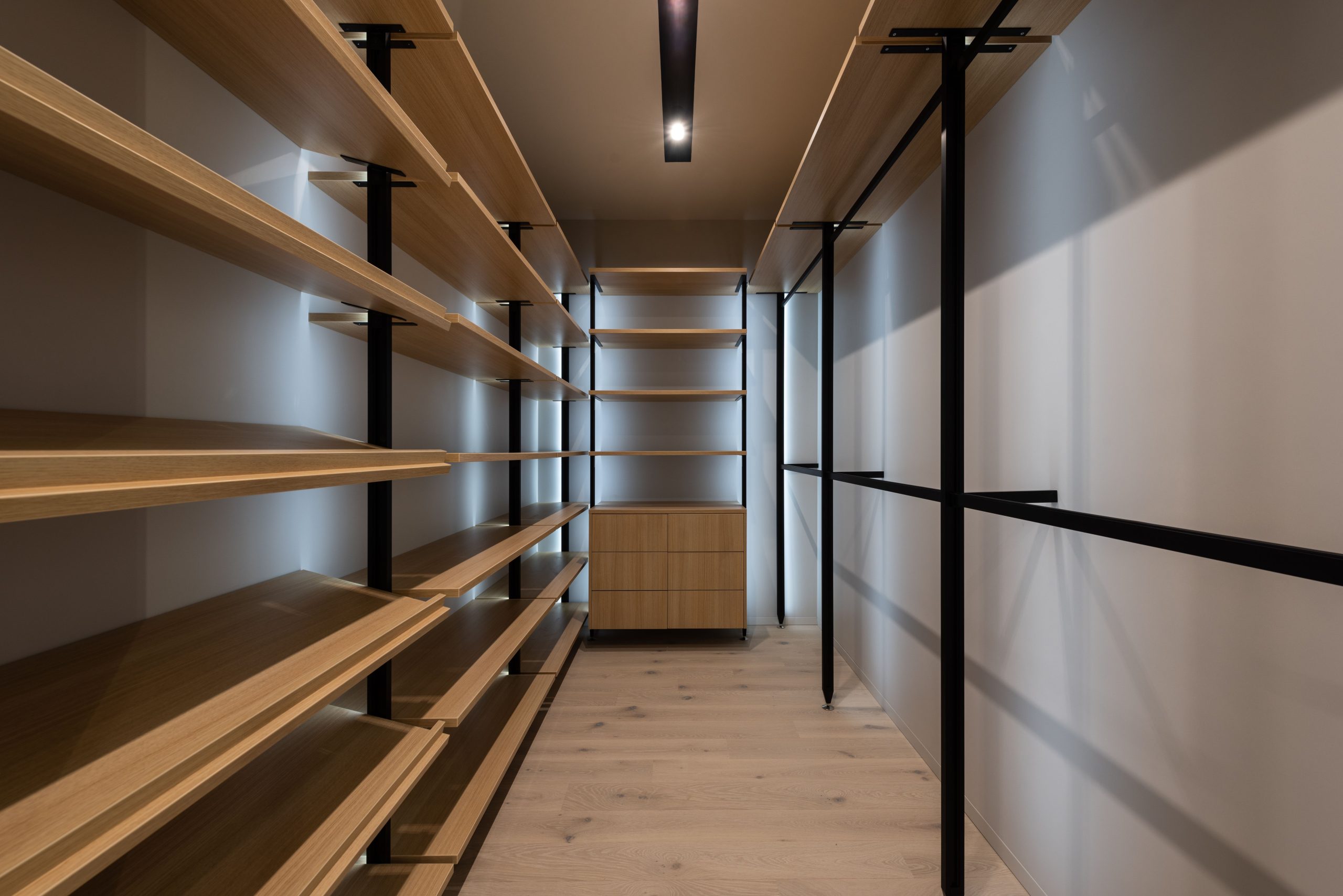 Interior of walk in closet with empty wooden shelves and railings in modern apartment