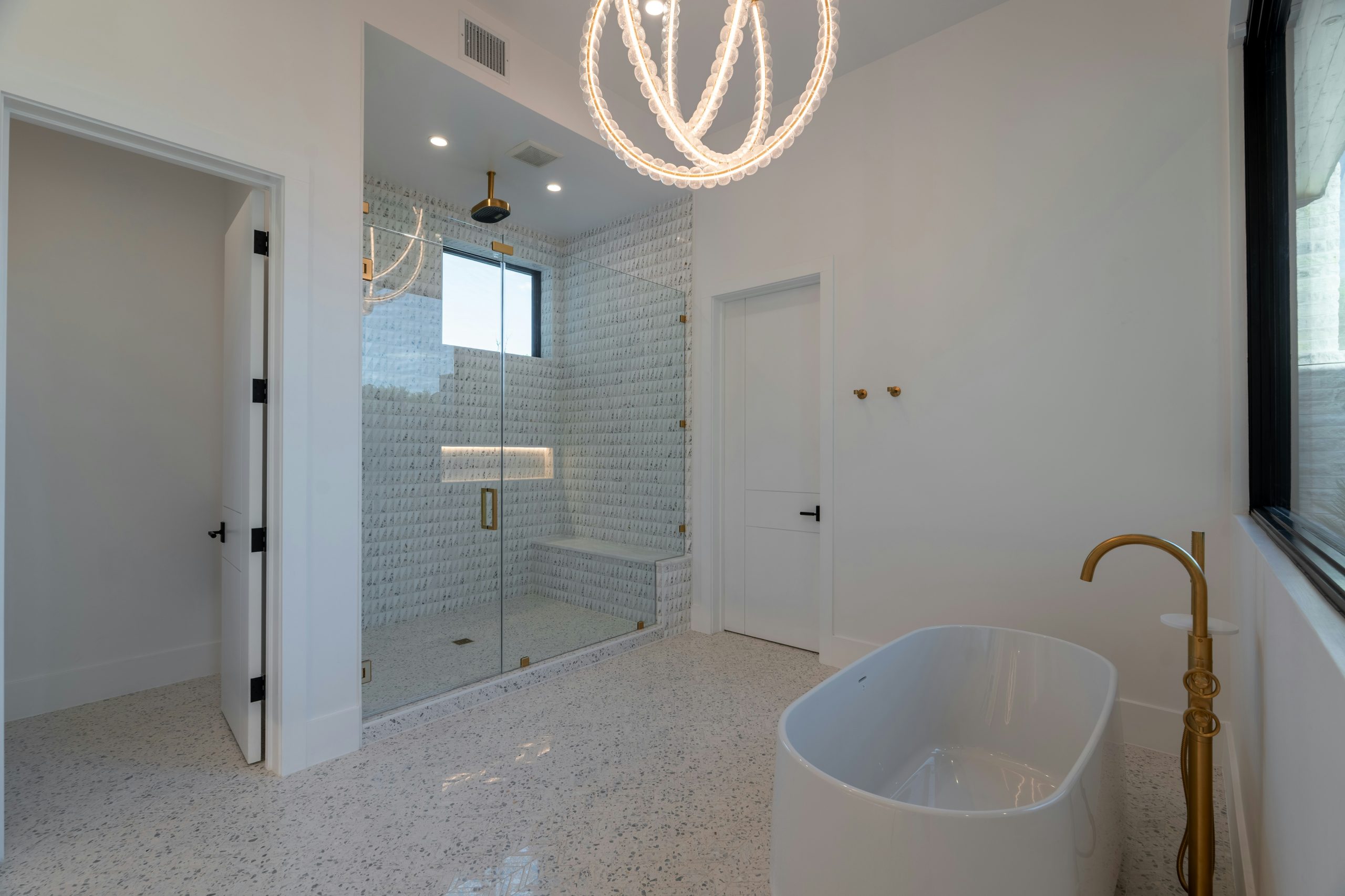 Modern white bathroom with freestanding tub and glass shower.
