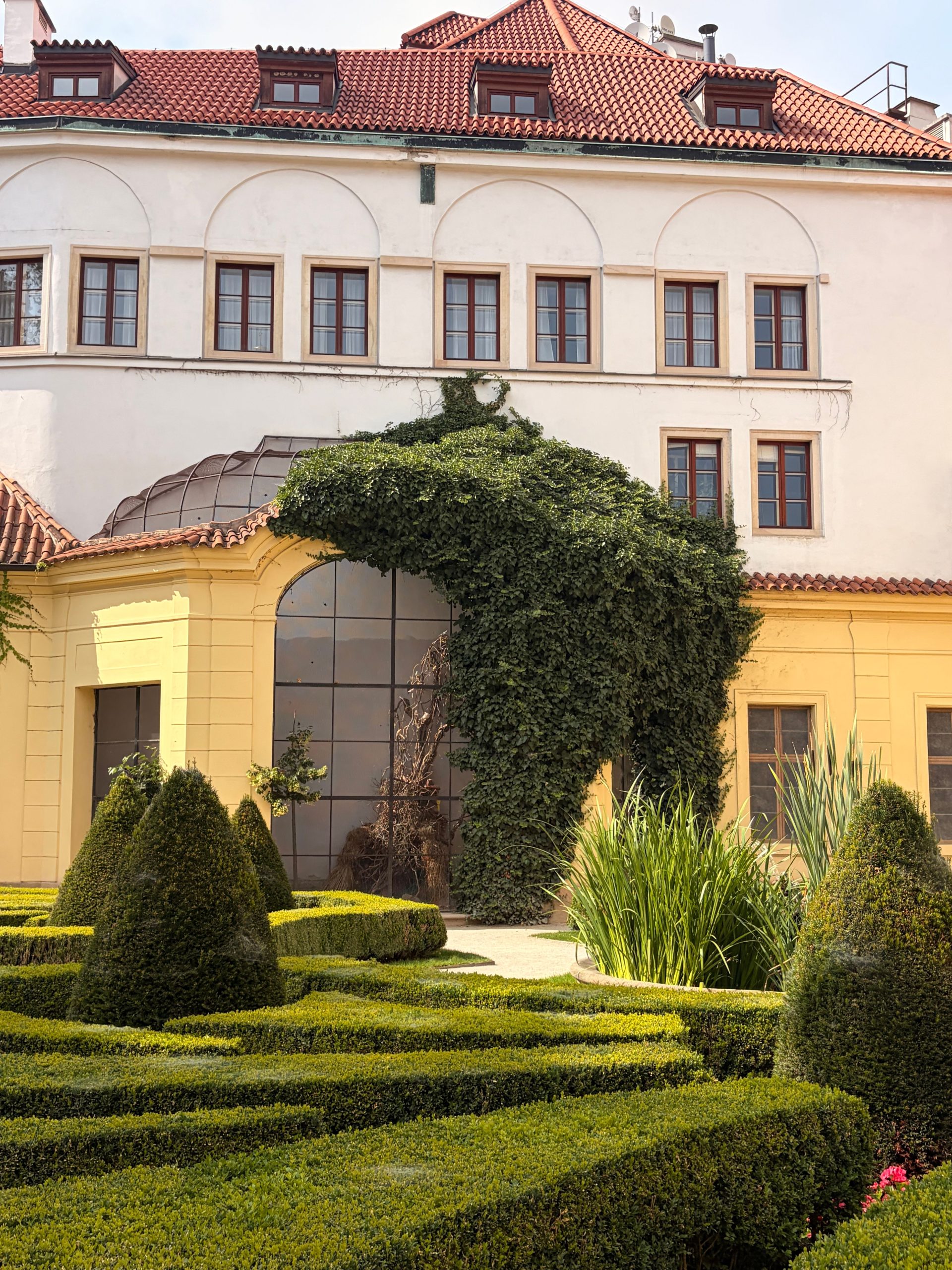 Stunning garden landscape featuring a beautifully pruned hedge and ivy-covered architecture in Prague.