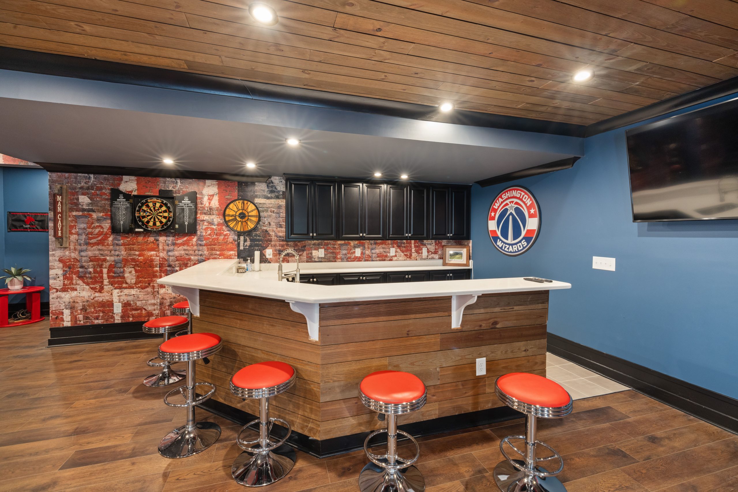 Stylish home bar with vibrant decor, featuring a Washington Wizards theme, dart board, and red bar stools.