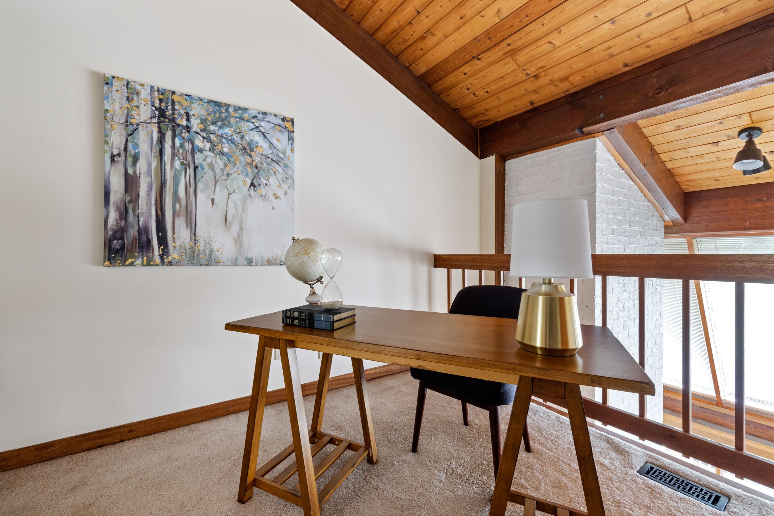 Stylish home office with wooden desk, chair, and artwork under vaulted ceilings.
