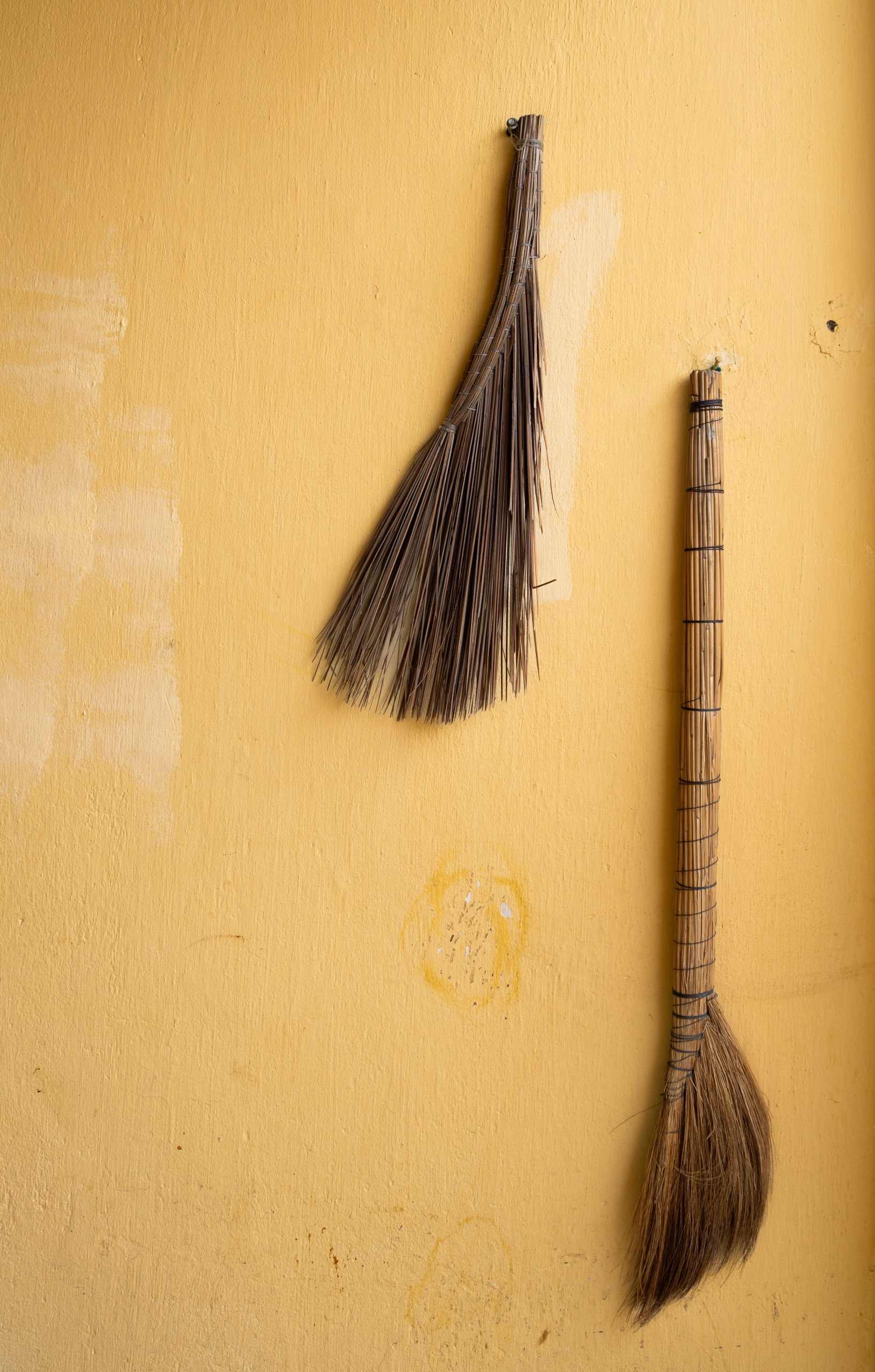 Traditional Vietnamese brooms against a weathered yellow wall, highlighting rural charm.