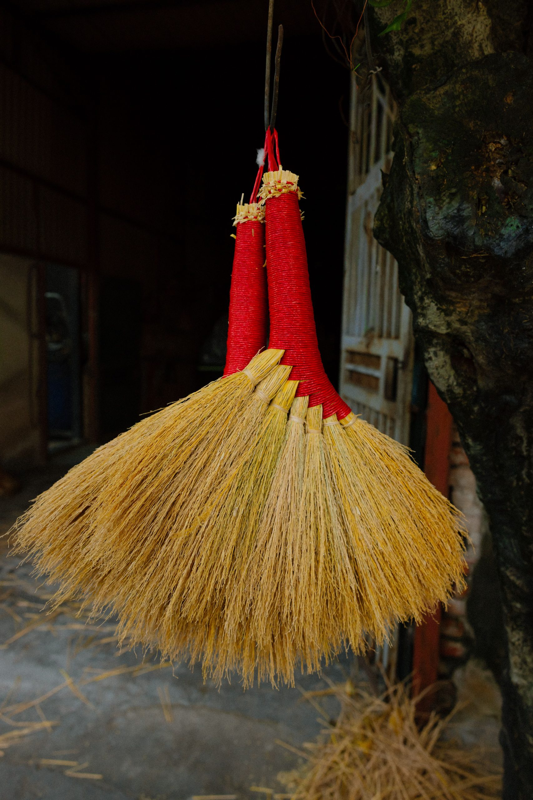 Two handcrafted red brooms hanging in a traditional workshop setting, showcasing artisanal craft.
