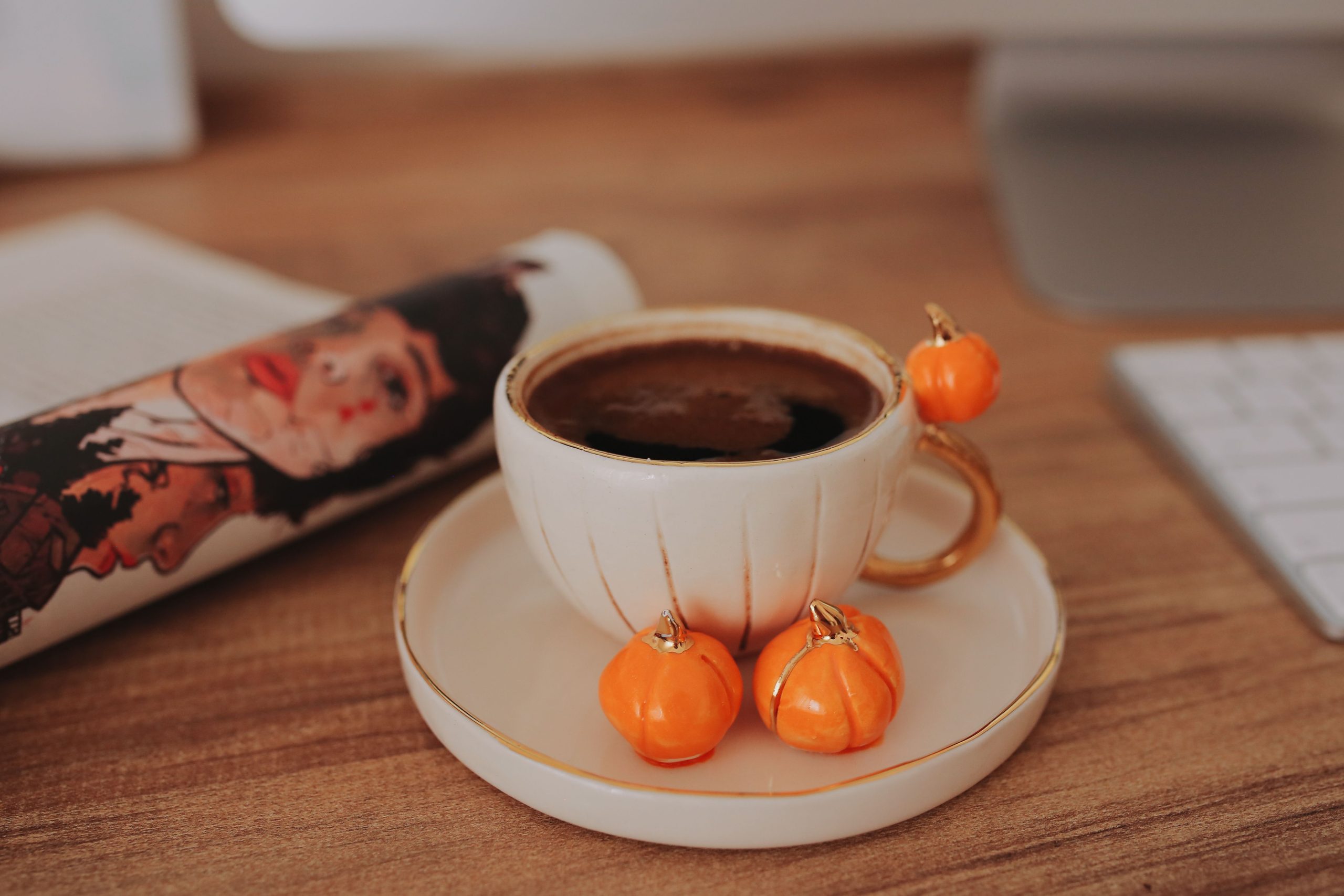 A close-up of a ceramic cup filled with black coffee, adorned with small pumpkins on a wooden surface.