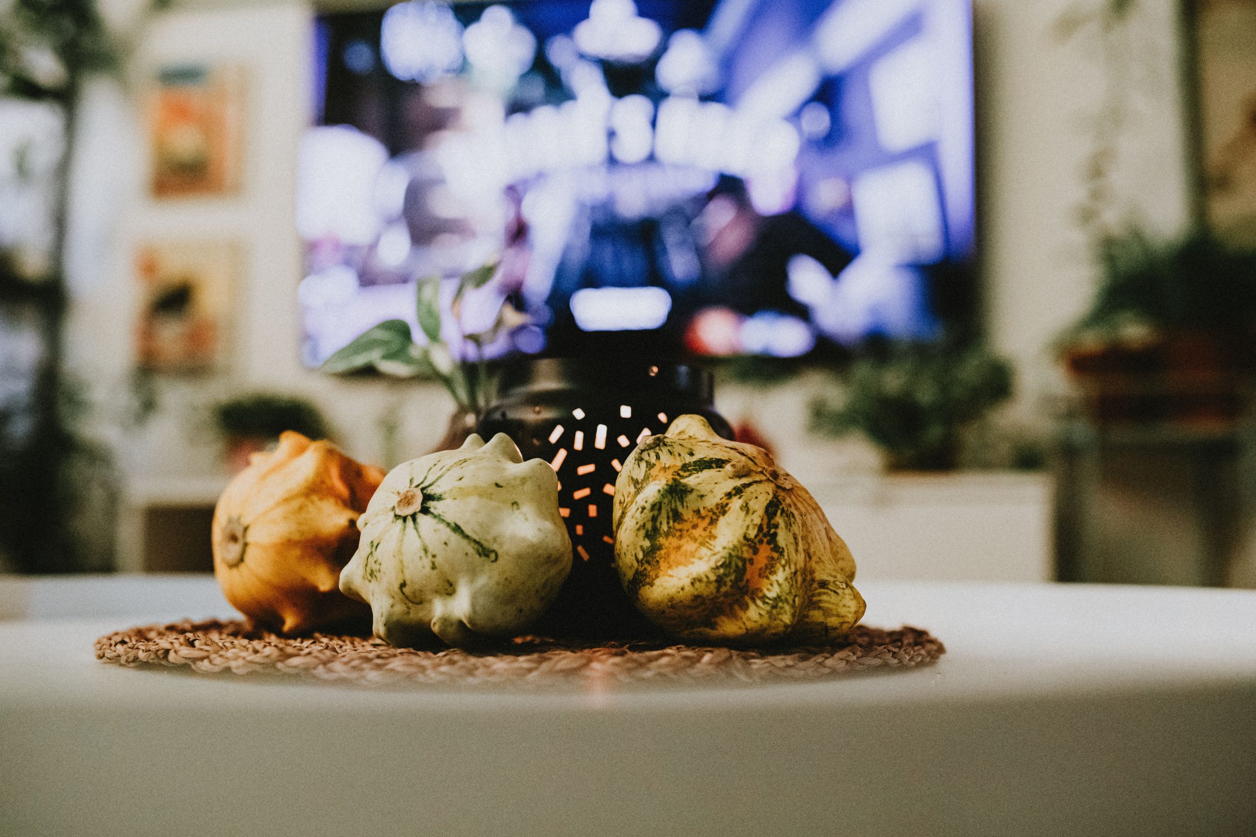 A cozy indoor setting featuring decorative gourds on a woven mat with a blurred television background.
