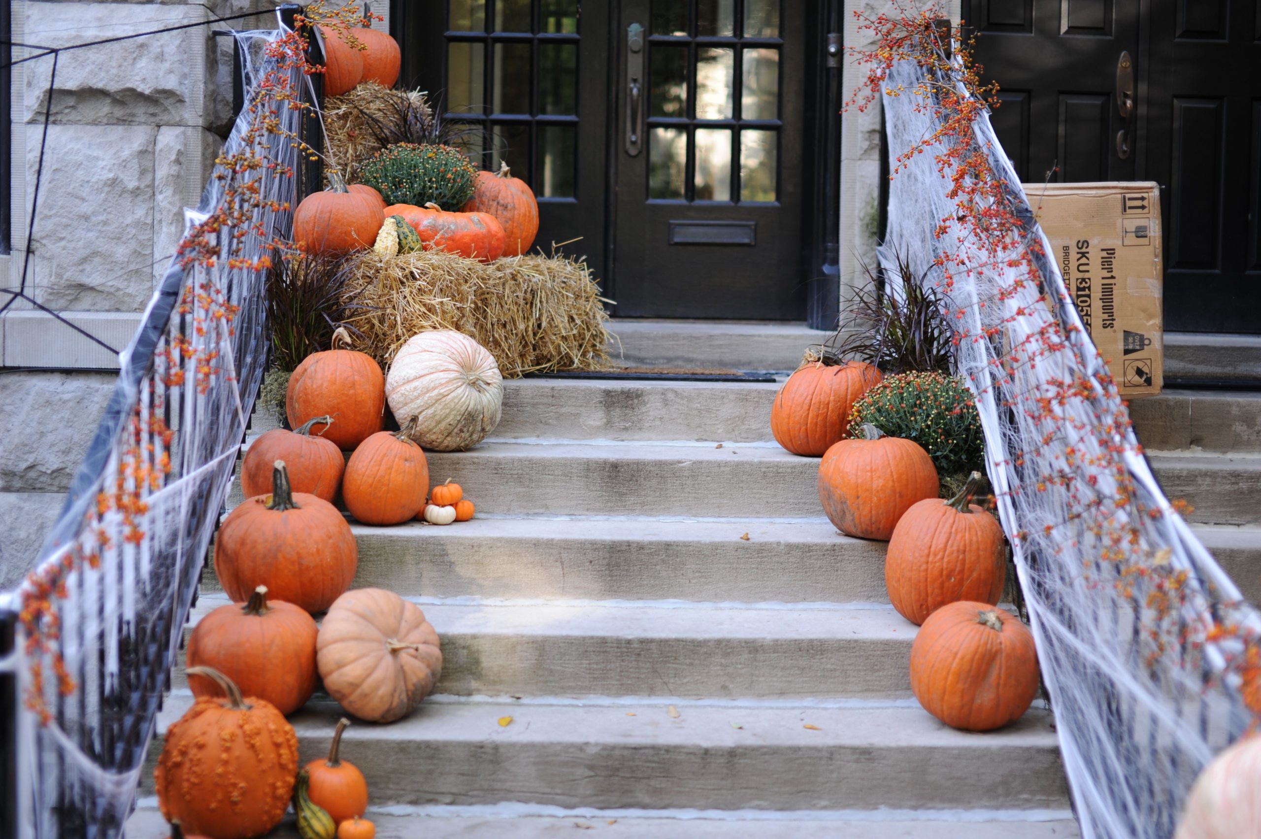 A front porch decorated with pumpkins and spider webs, celebrating Halloween and fall season.