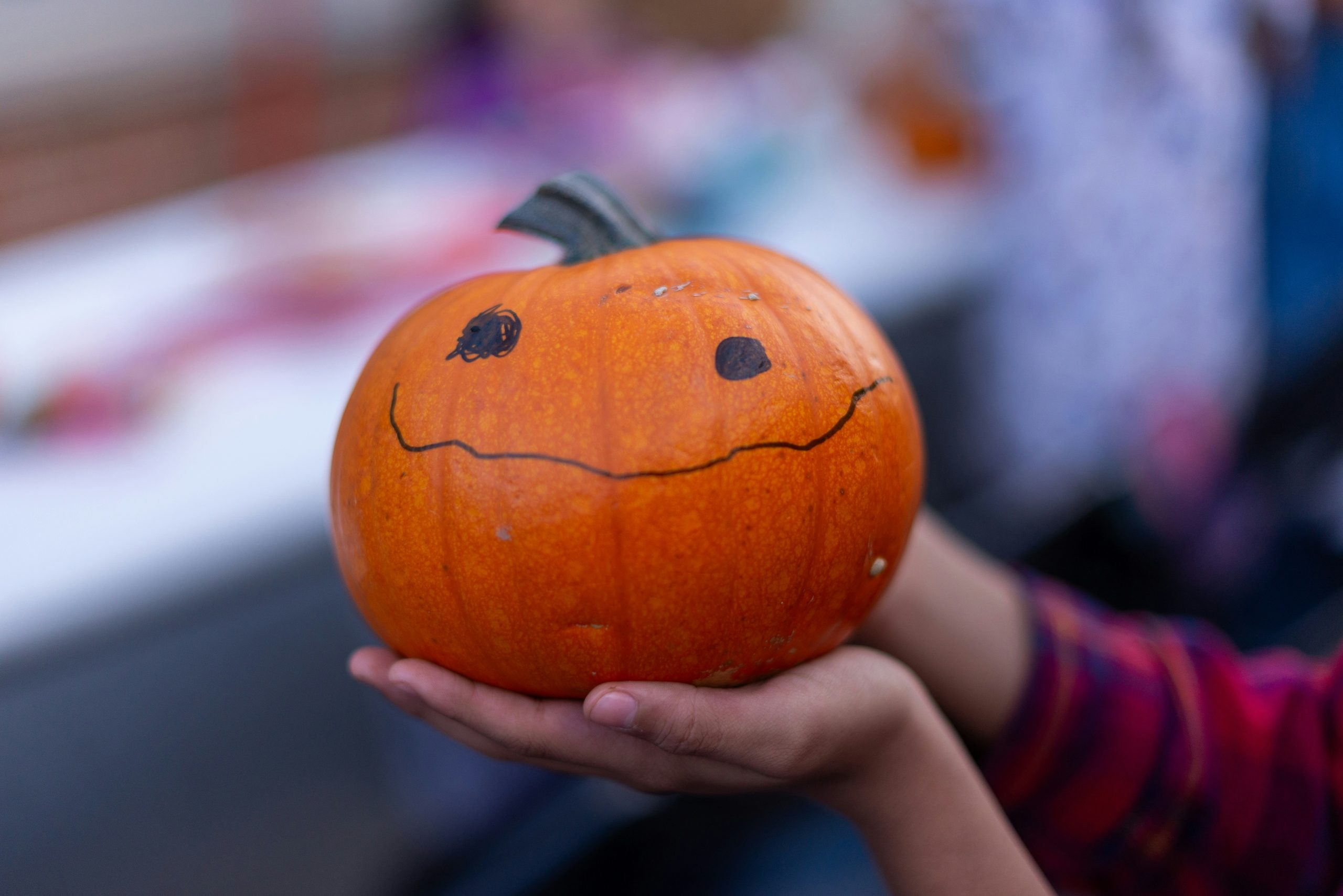 a person holding a pumpkin with a smiley face drawn on it