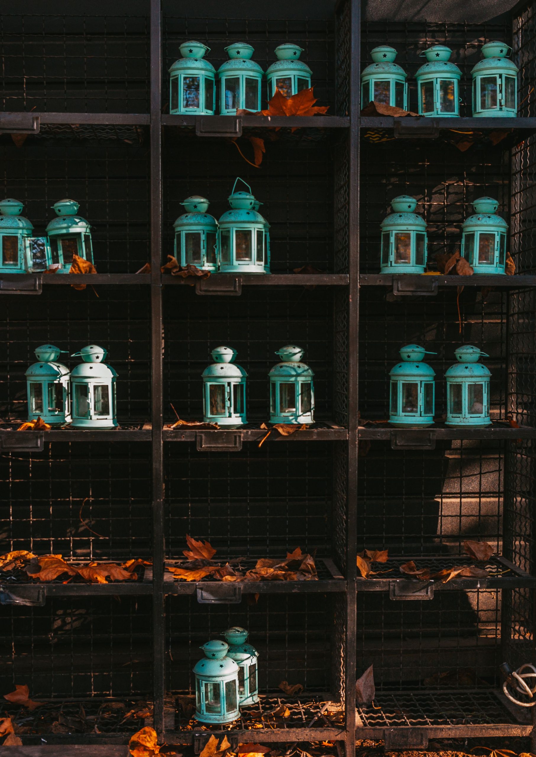 A row of teal lanterns on a shelf with dried autumn leaves, creating a rustic vibe.