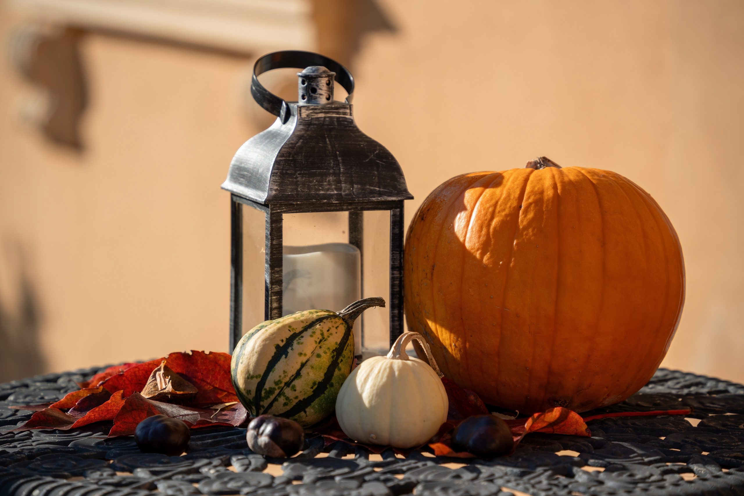 A rustic autumn arrangement with pumpkins, leaves, and a lantern on a table.
