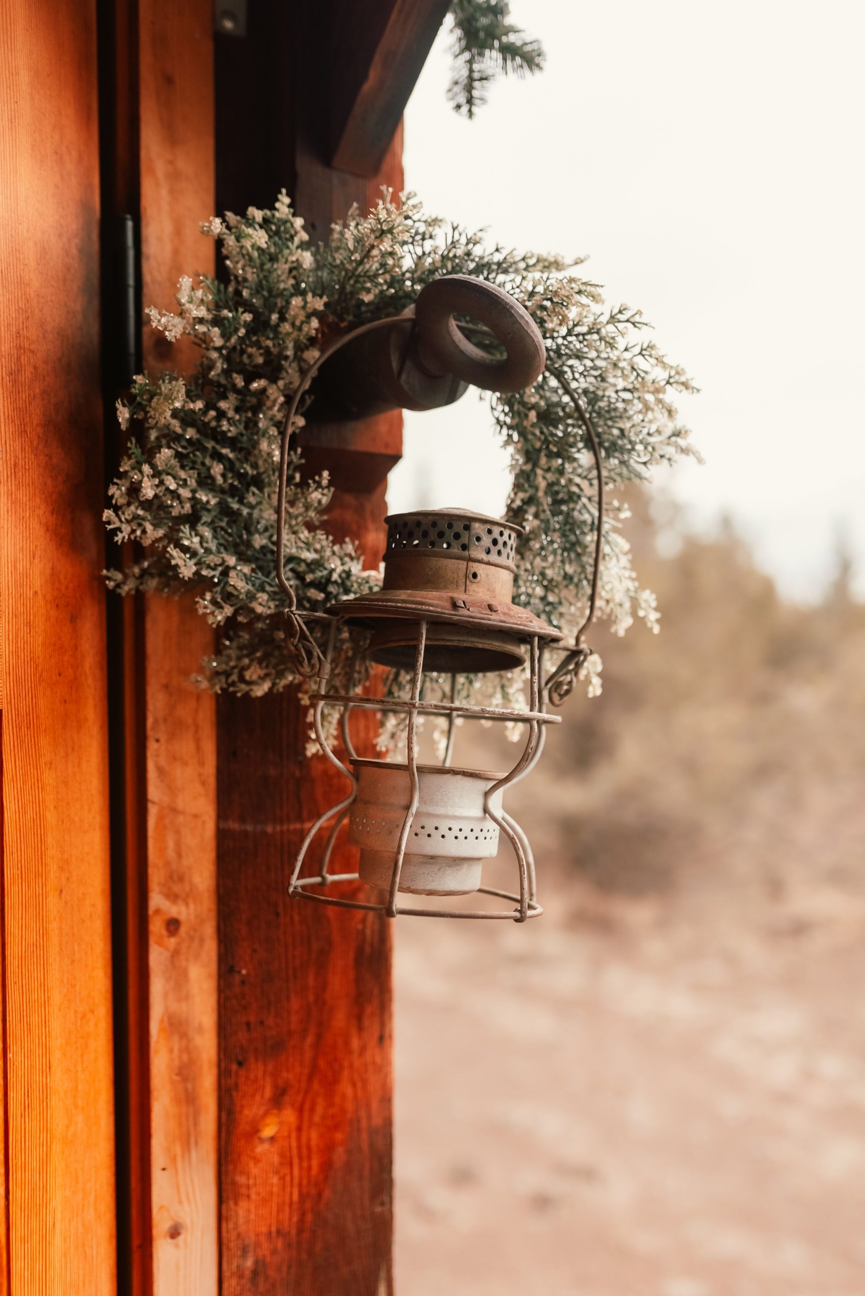 A rustic lantern hangs on a wooden wall with a floral wreath, creating a cozy outdoor ambiance.