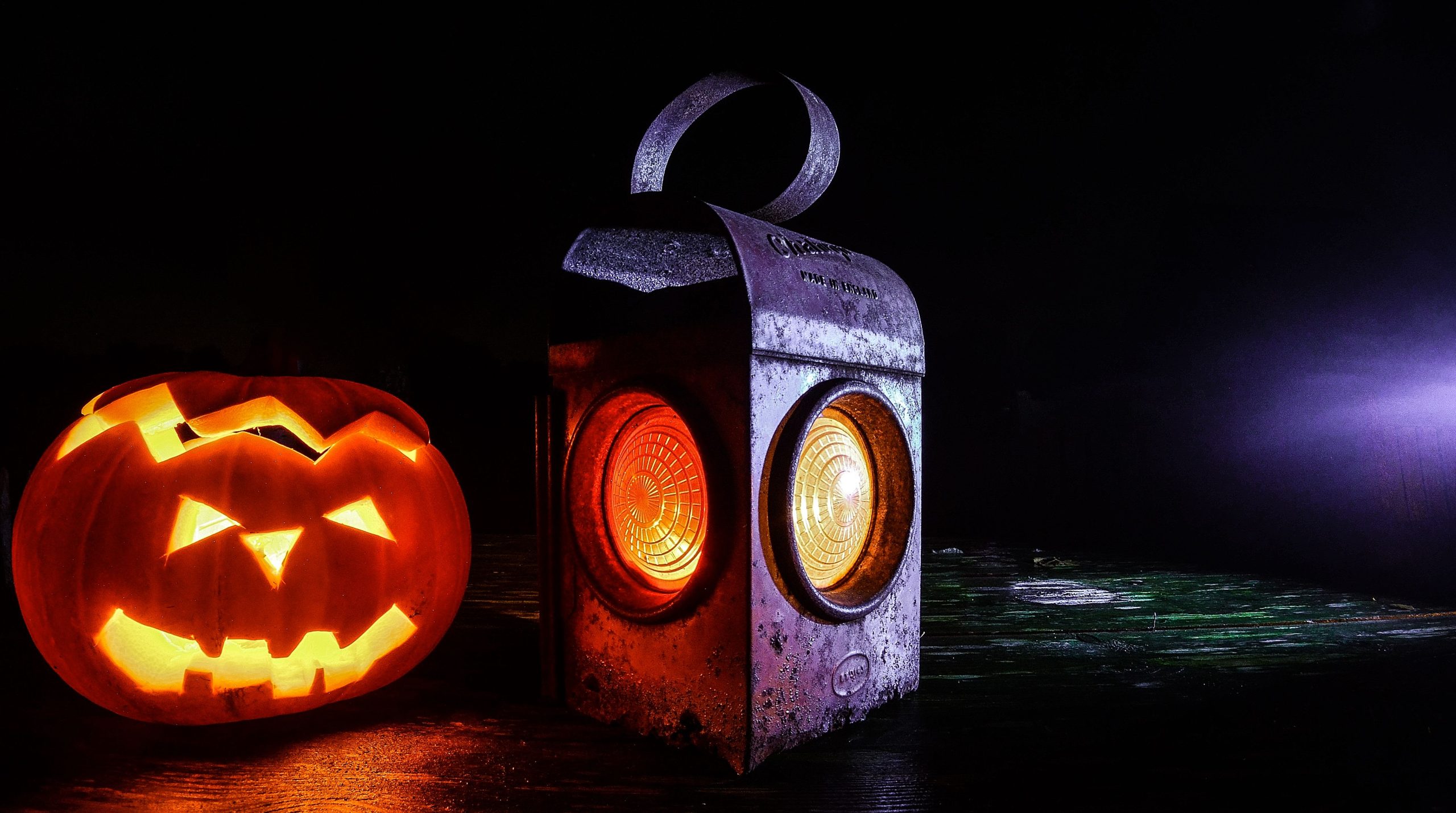 A spooky Halloween scene with a glowing jack-o'-lantern and vintage lantern on a dark background.