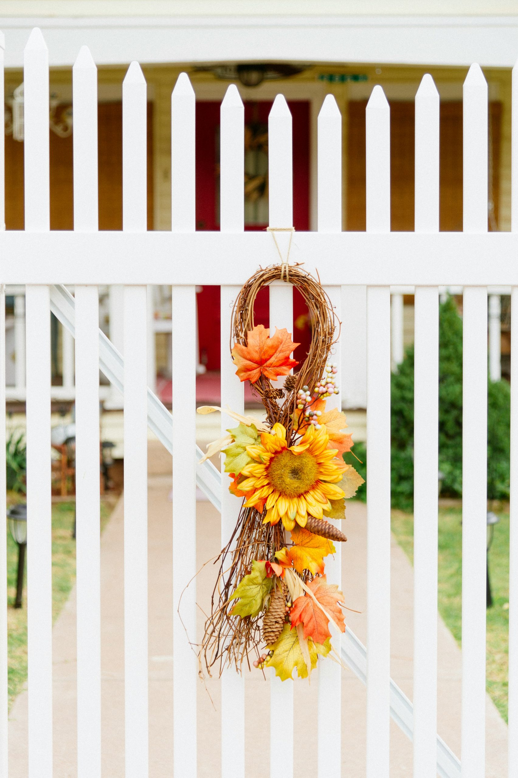 a sunflower wreath hangs on a white picket fence