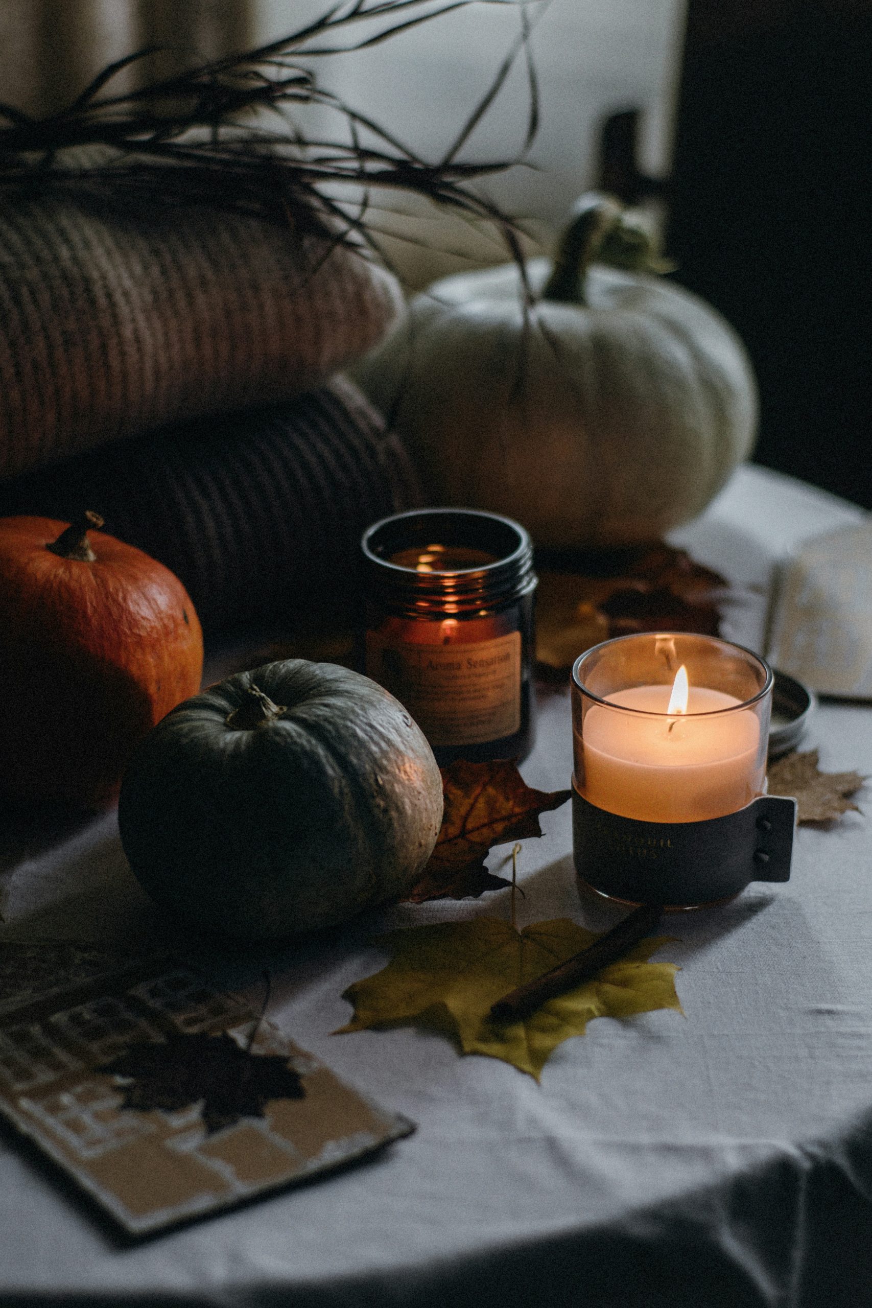 a table topped with a candle next to a pile of pumpkins