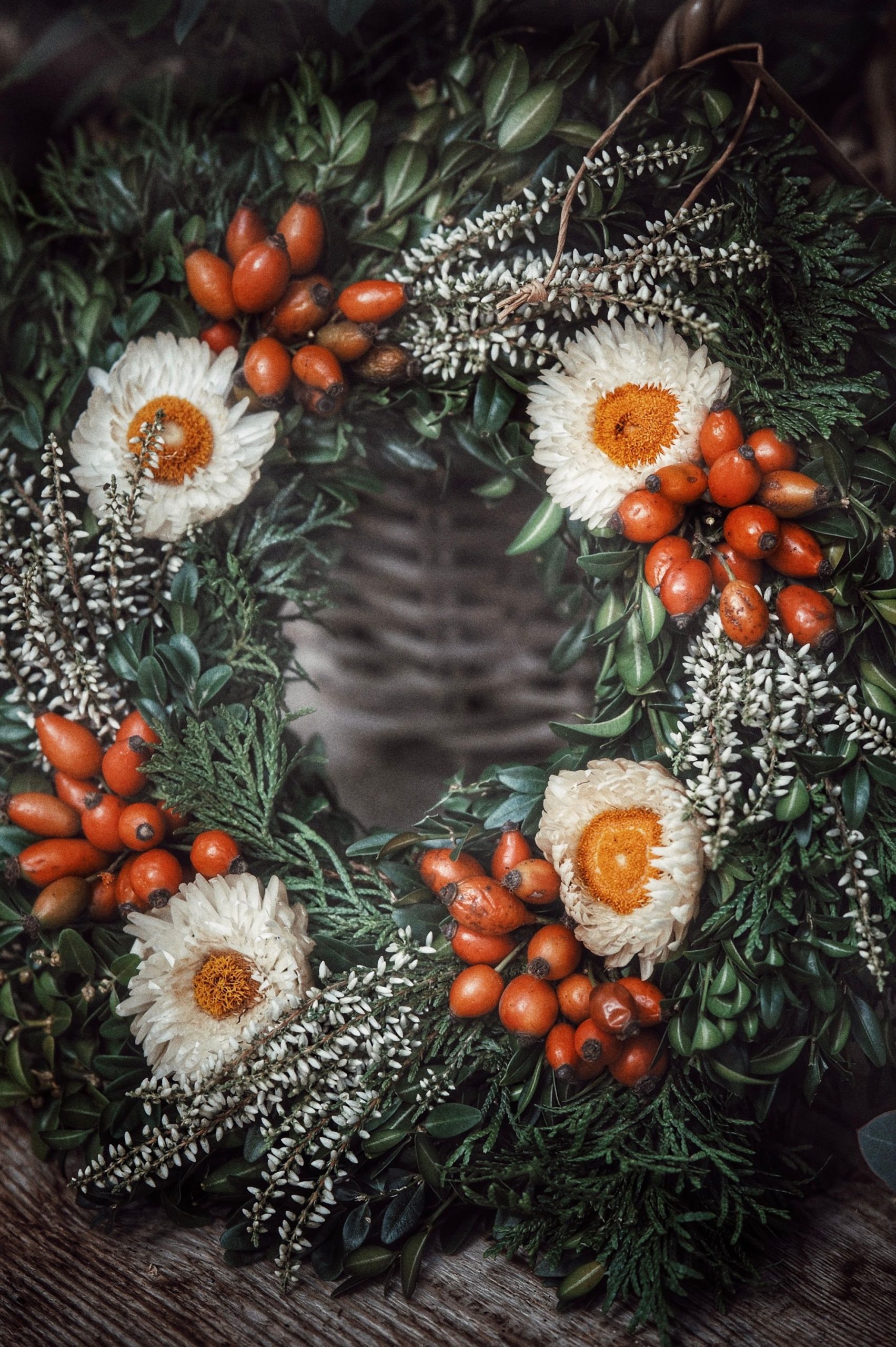 A vibrant floral wreath featuring red berries and white mimosas. Ideal for festive decor.