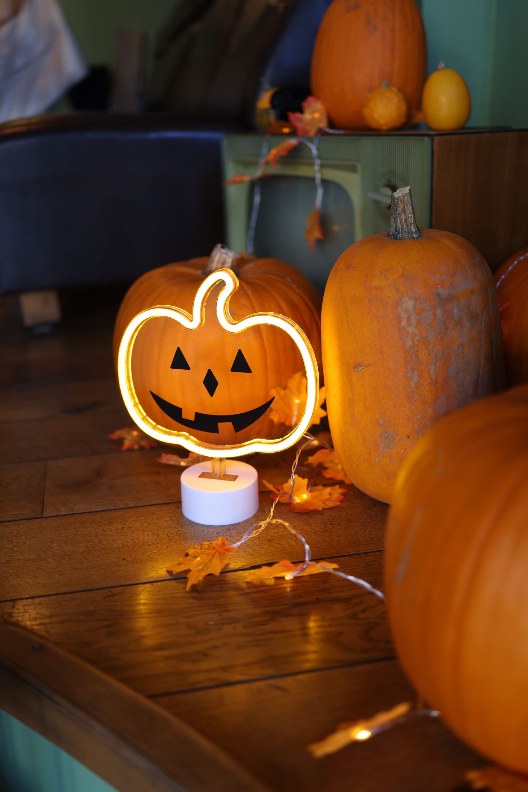A warm indoor scene featuring pumpkins, autumn leaves, and a Jack O' Lantern neon light.