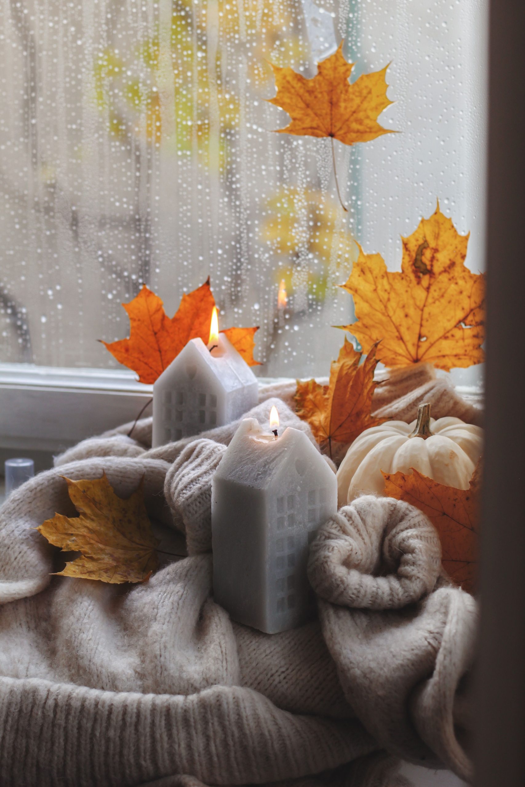A warm, inviting autumn scene with candles and leaves on a windowsill, creating a cozy ambiance.