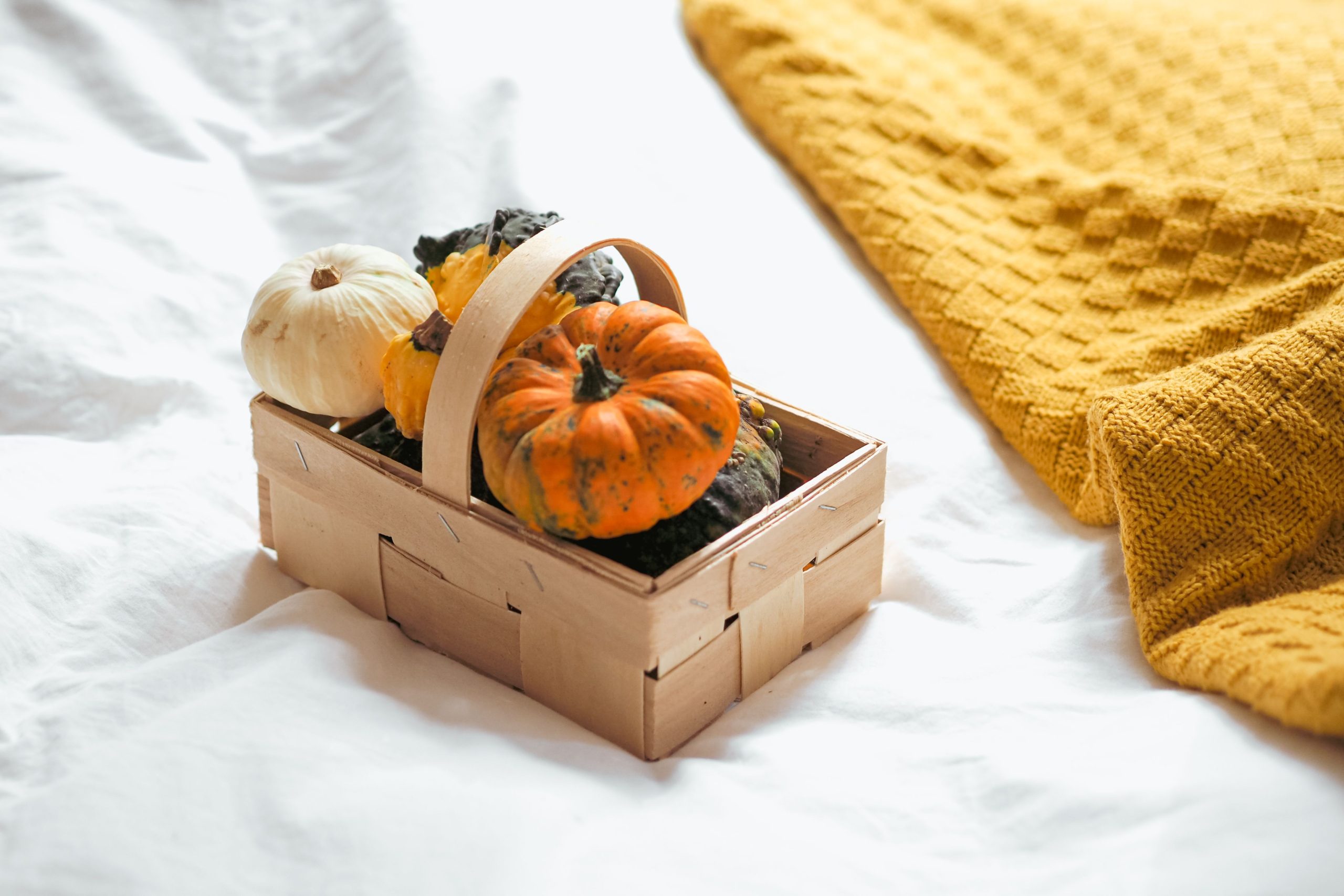 A wicker basket filled with pumpkins on a bed with a warm orange blanket, perfect for autumn vibes.