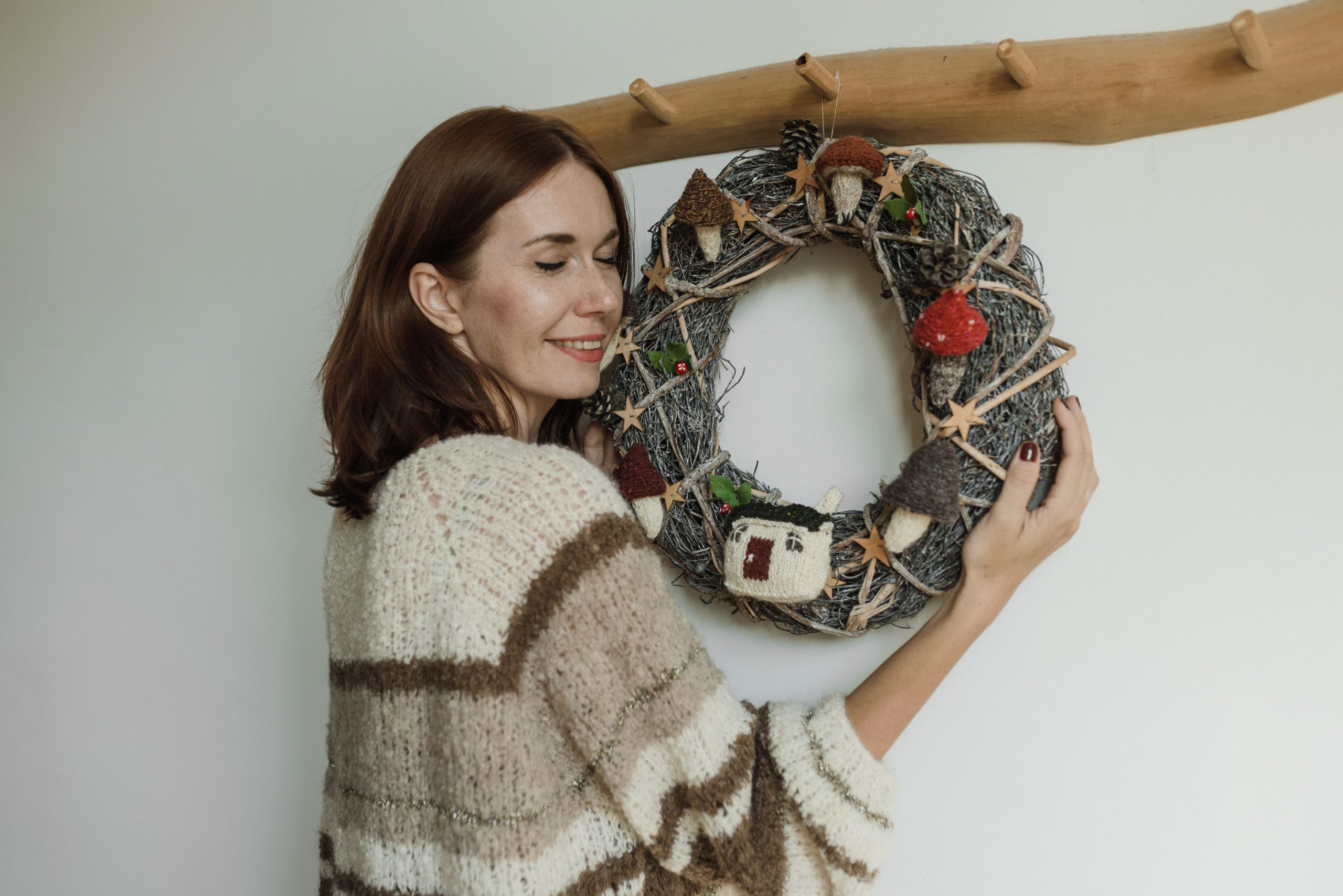 A woman joyfully embraces a rustic handmade wreath decorated with knitted elements and natural textures.