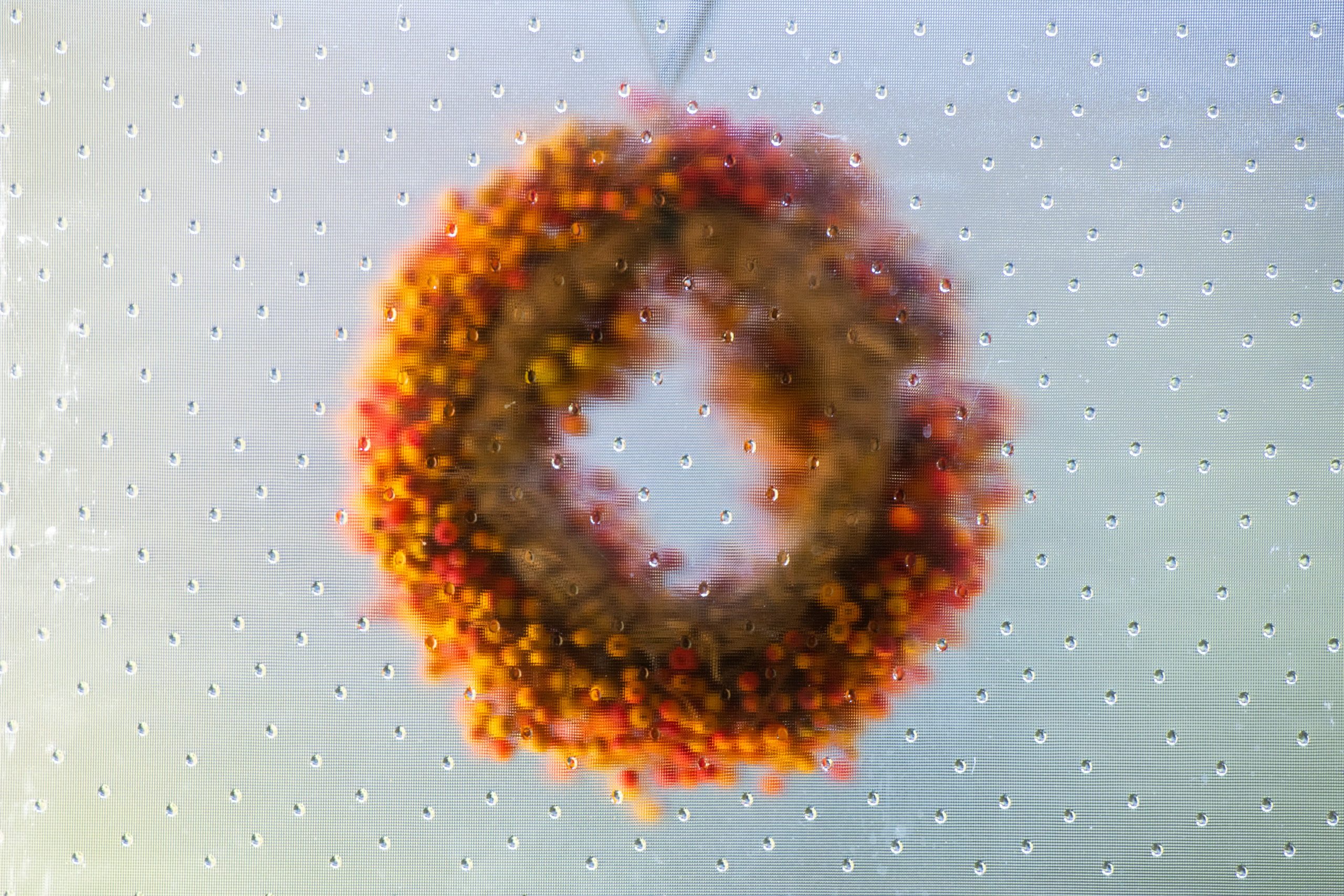 An artistic view of a colorful autumn wreath seen through raindrop-covered glass, evoking a cozy seasonal mood.