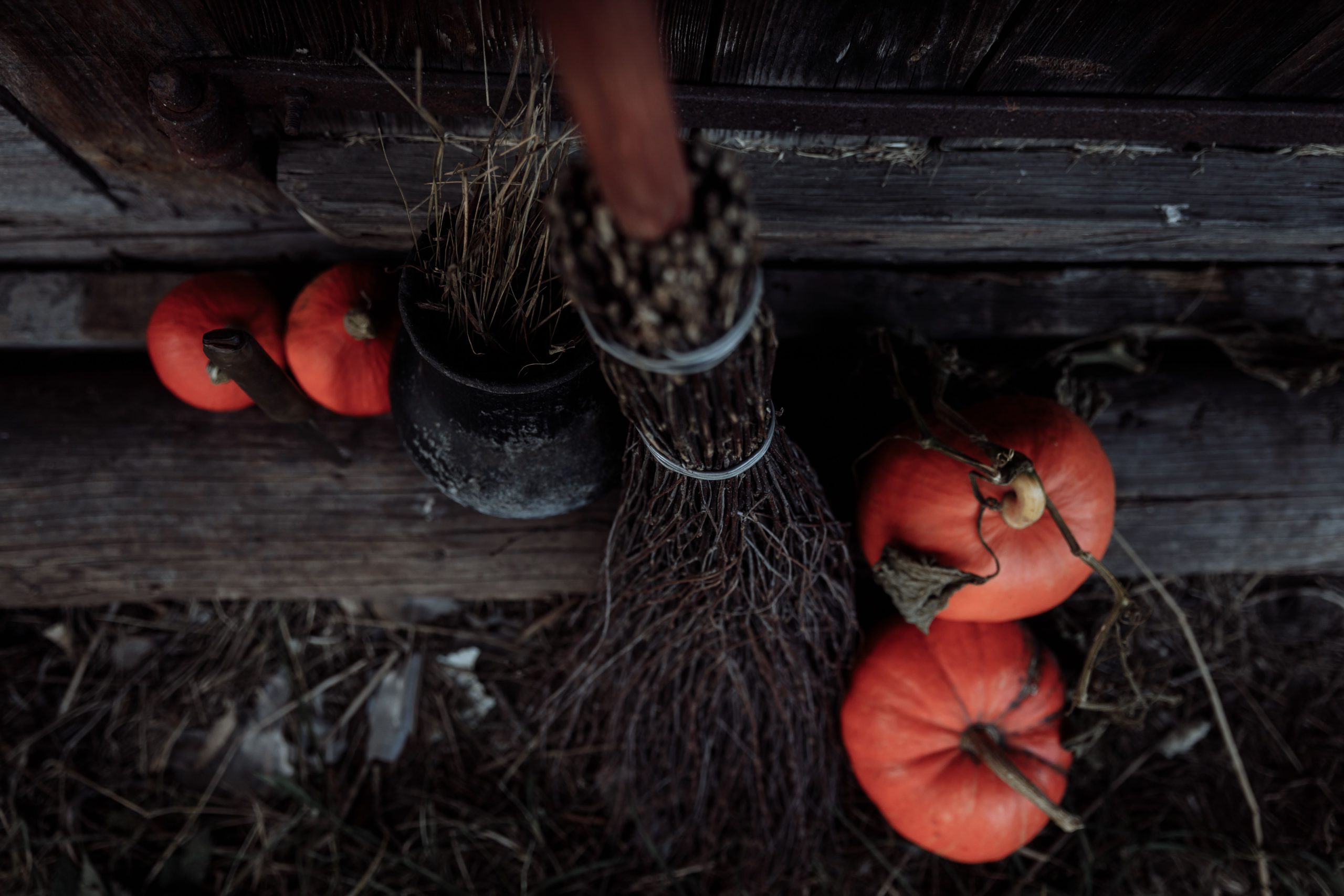 An atmospheric Halloween setup with a witch's broom and pumpkins against a rustic wooden backdrop.
