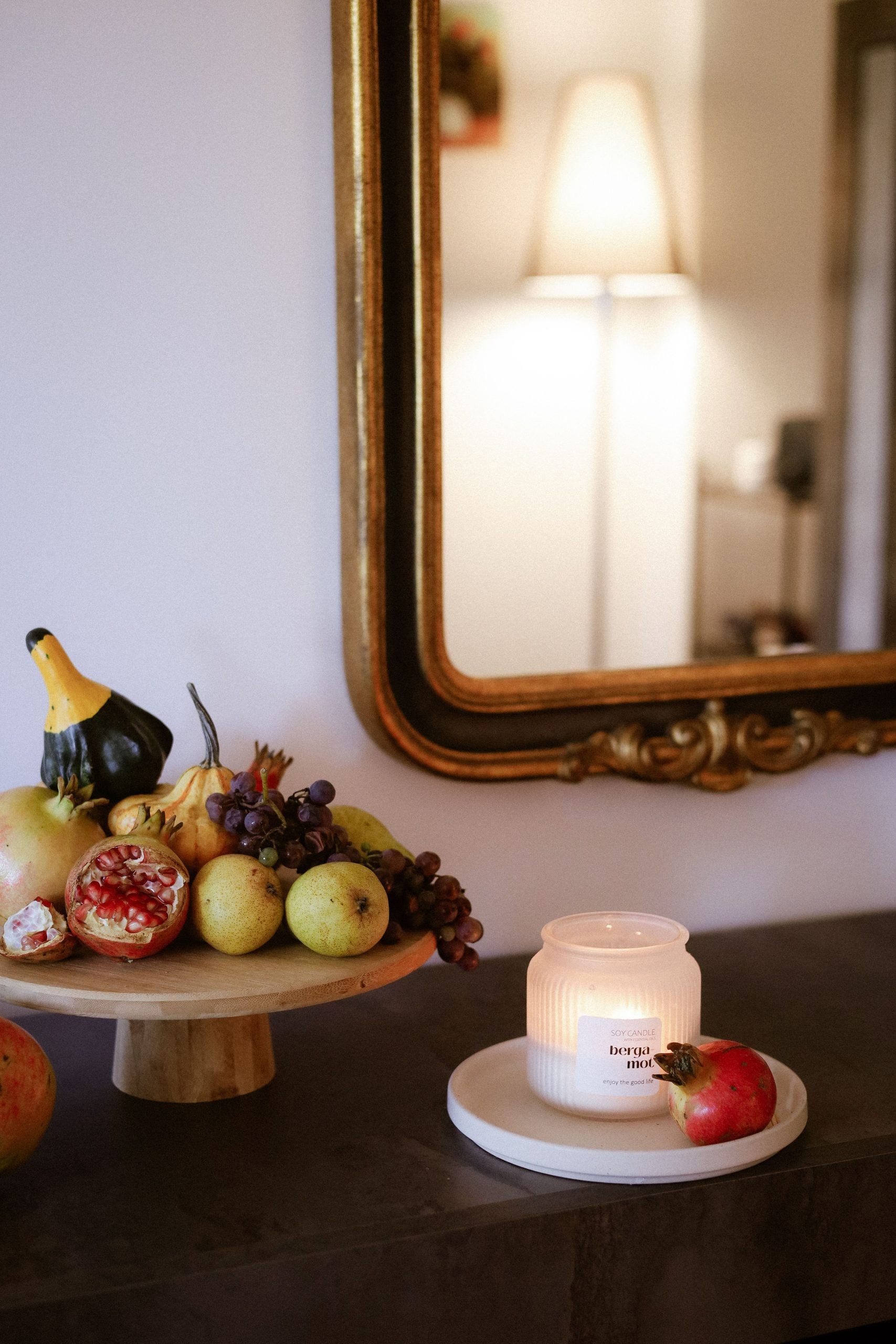 Arrangement of autumn fruits and a lit candle in a warm interior setting.