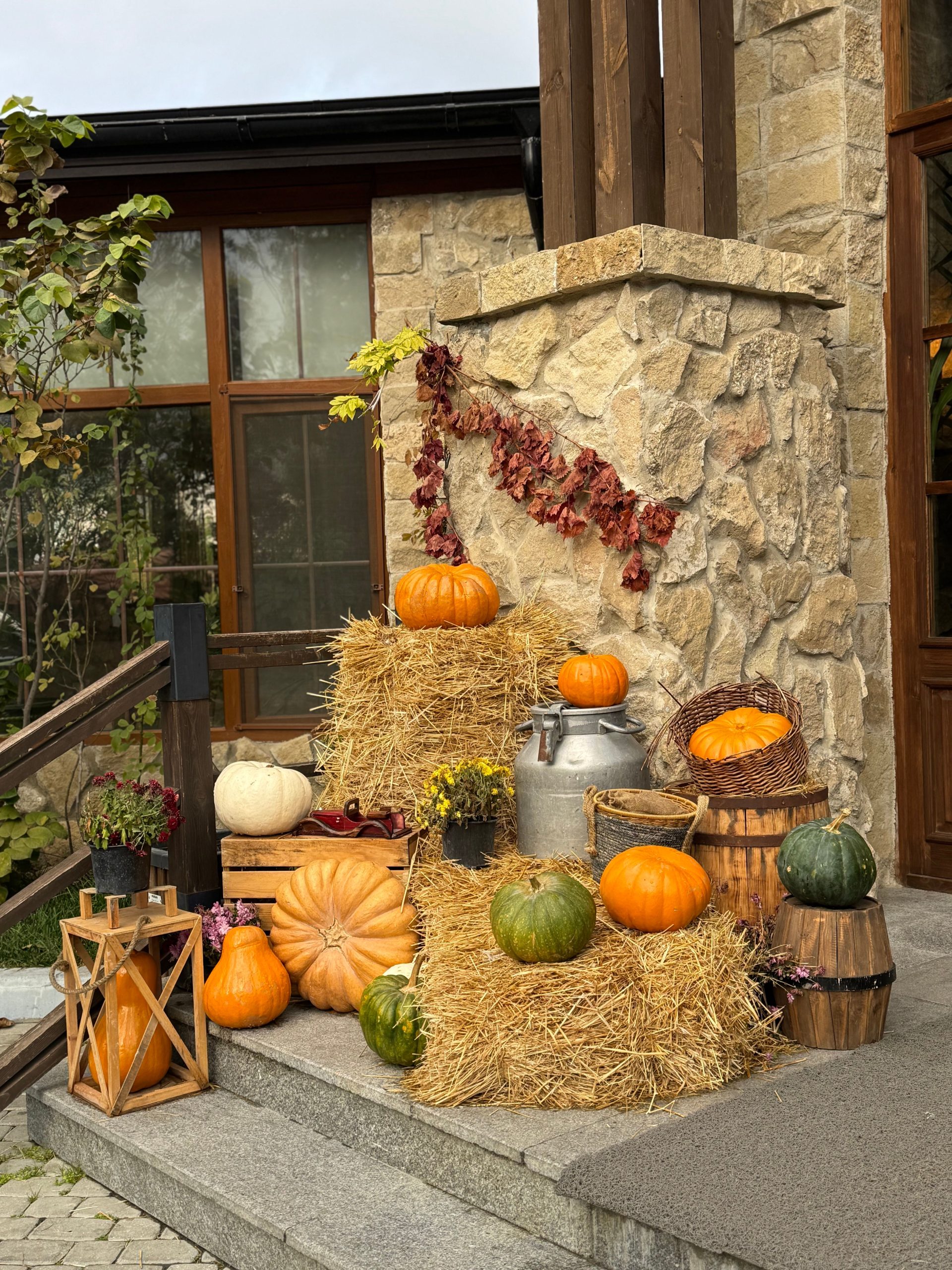 Autumn harvest scene featuring pumpkins, hay bales, and dried leaves by a stone building.