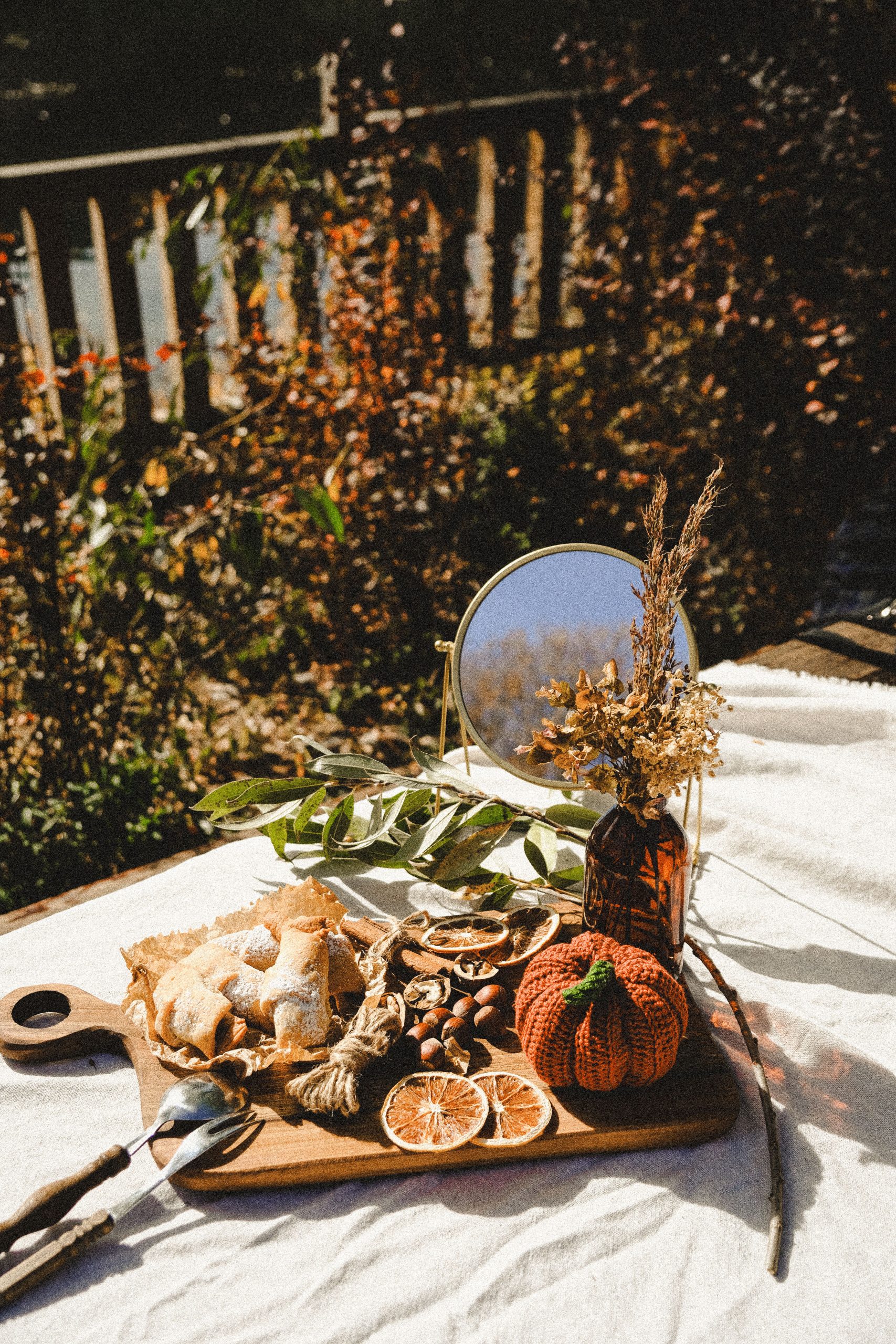 Autumn-themed still life featuring dried citrus, pastries, and decorations on a cutting board outdoors.