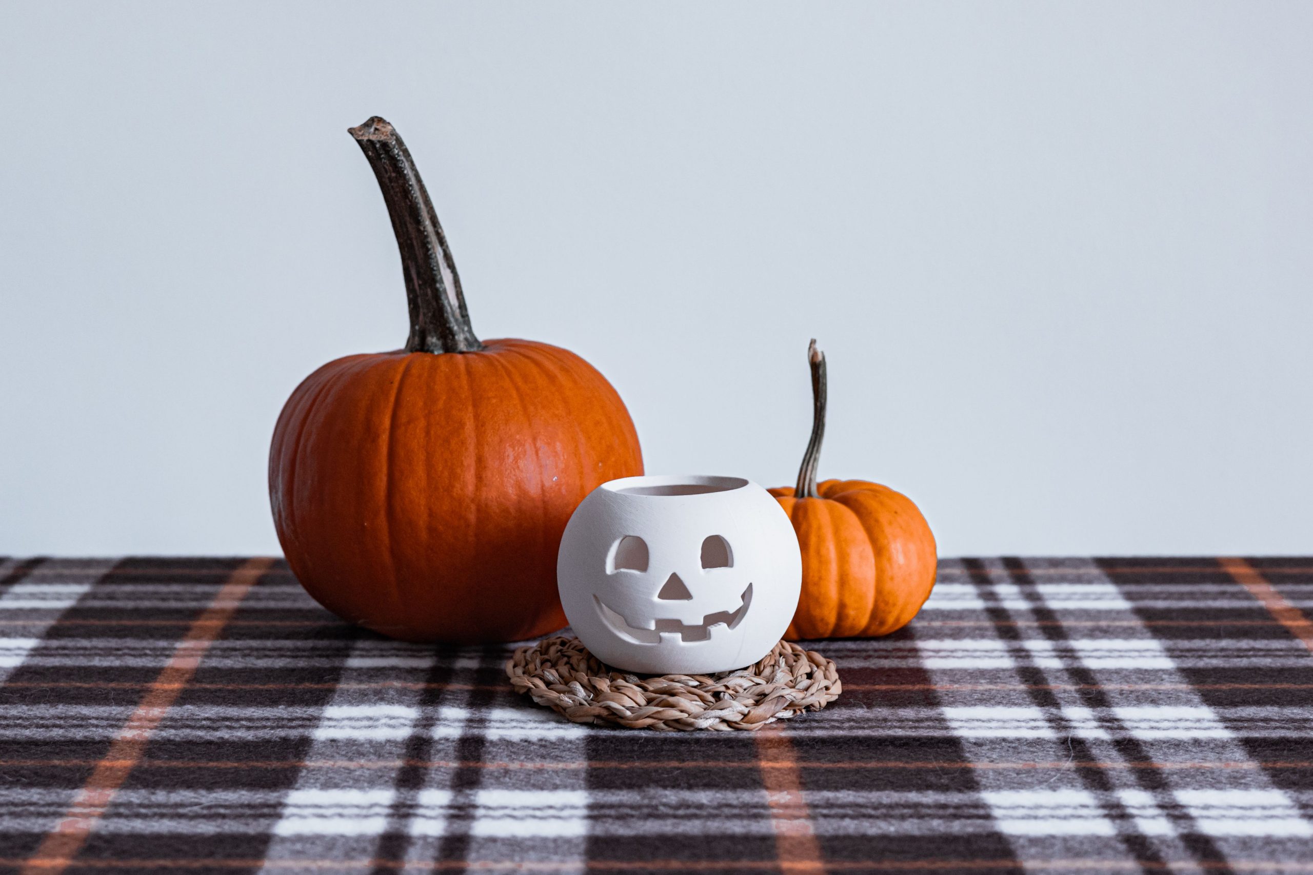 Autumn-themed still life featuring orange pumpkins and a carved candle holder on a plaid tablecloth.