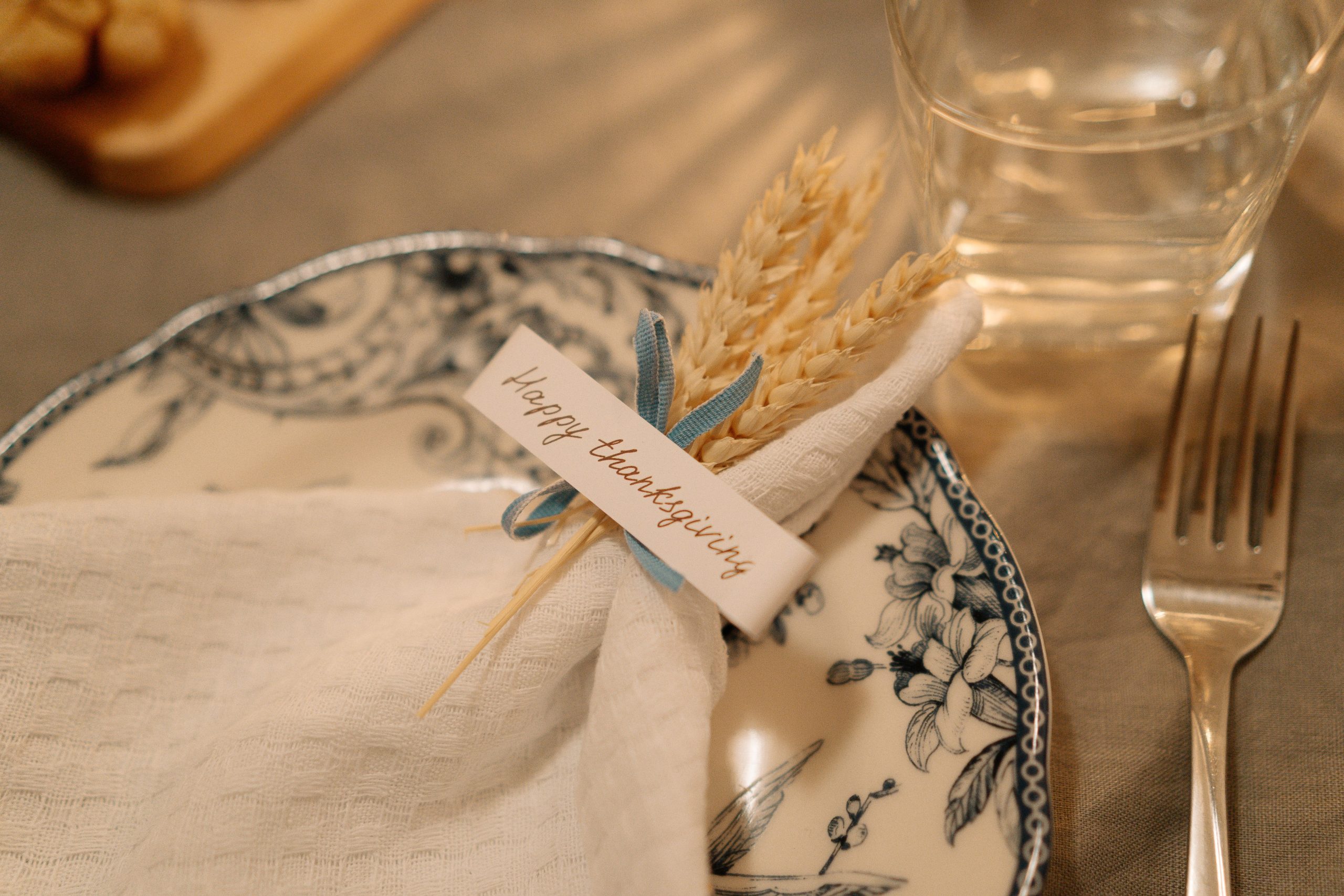 Beautiful Thanksgiving table setting with decorated plate and napkin featuring wheat and a festive greeting card.