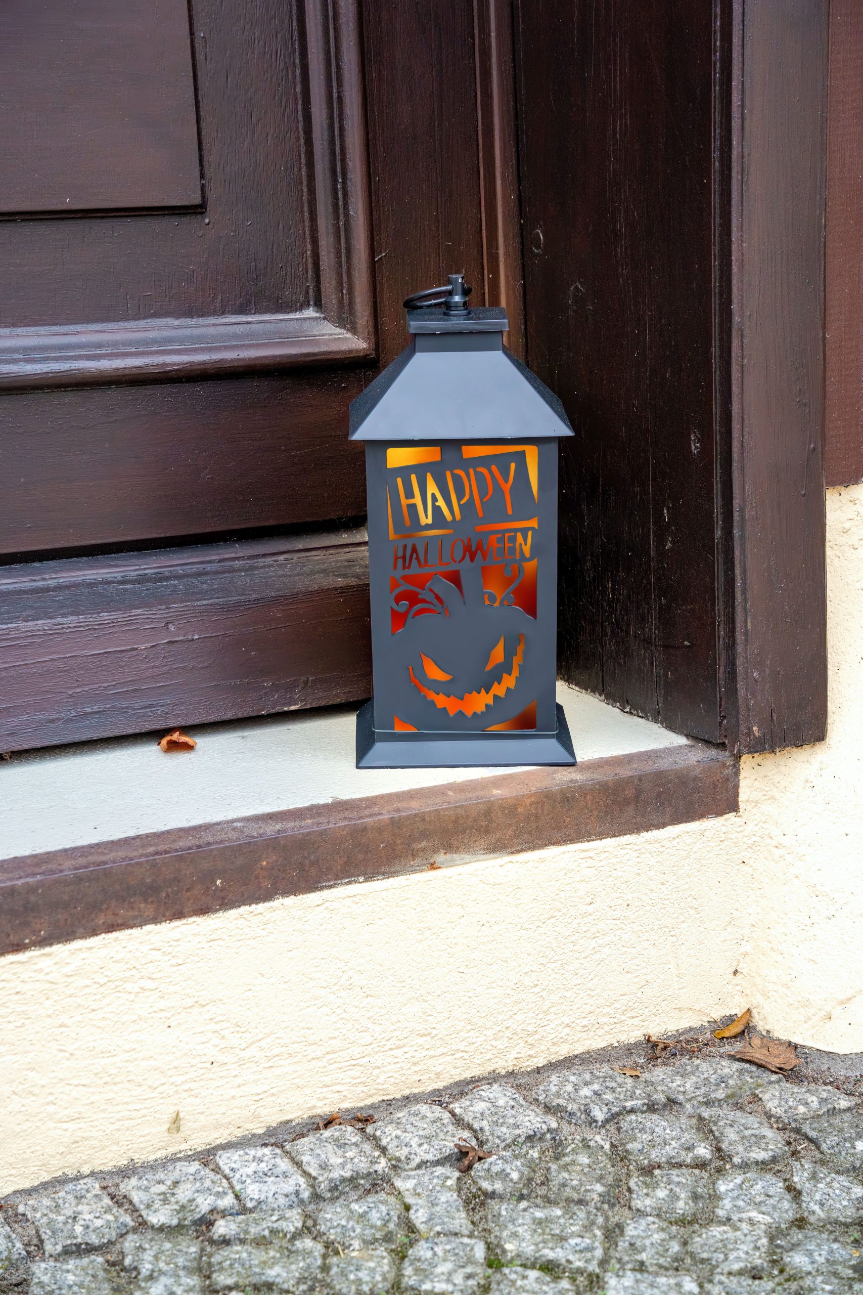 Black lantern with jack-o'-lantern design on a doorstep, perfect for Halloween decor.