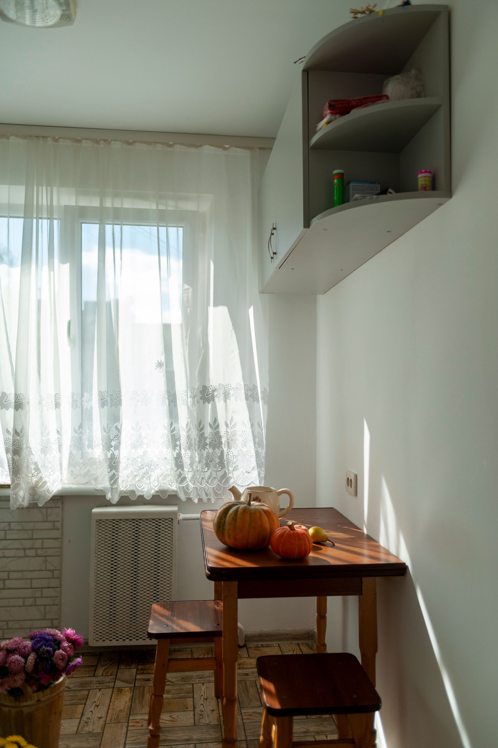 Bright kitchen with cozy decor, autumn pumpkins on table, and sunlight through window in Lviv, Ukraine.