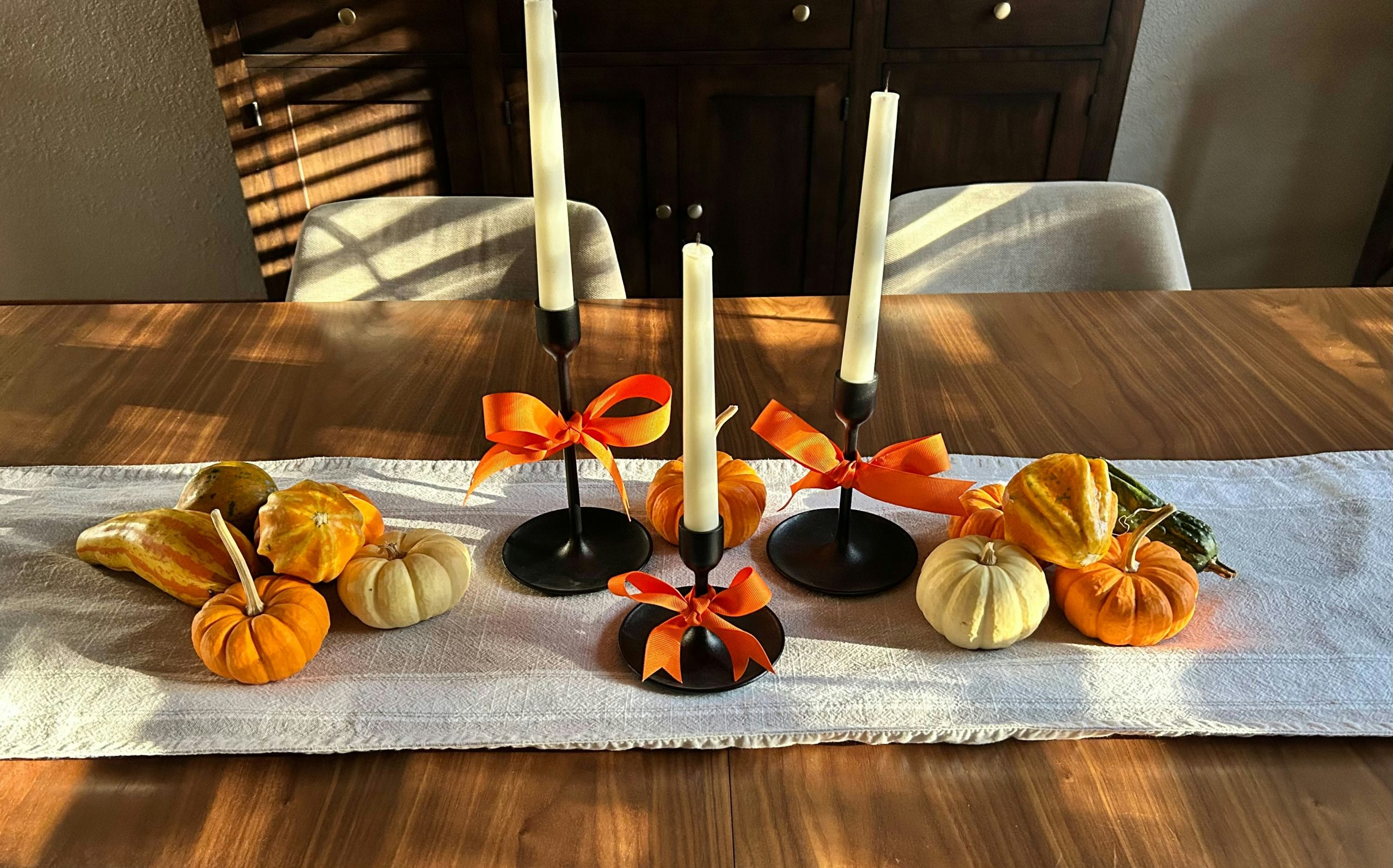 Candlesticks with pumpkins and gourds on a table runner