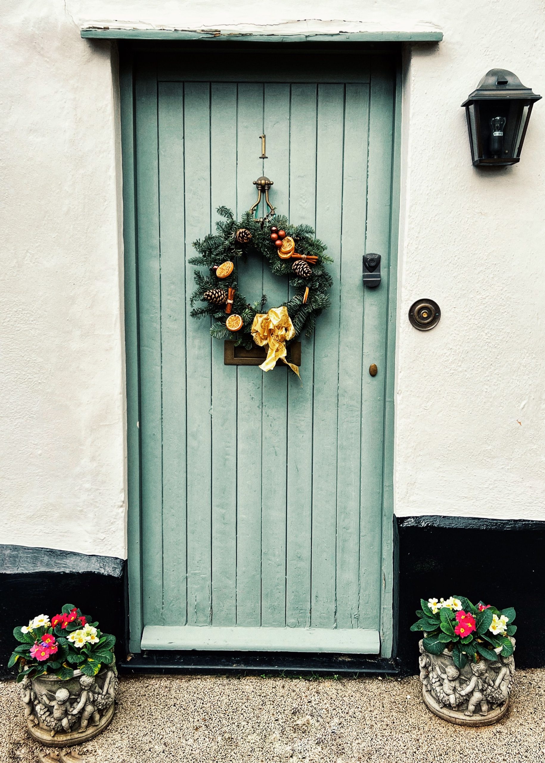 Charming green wooden door with a festive wreath, framed by colorful flower pots.