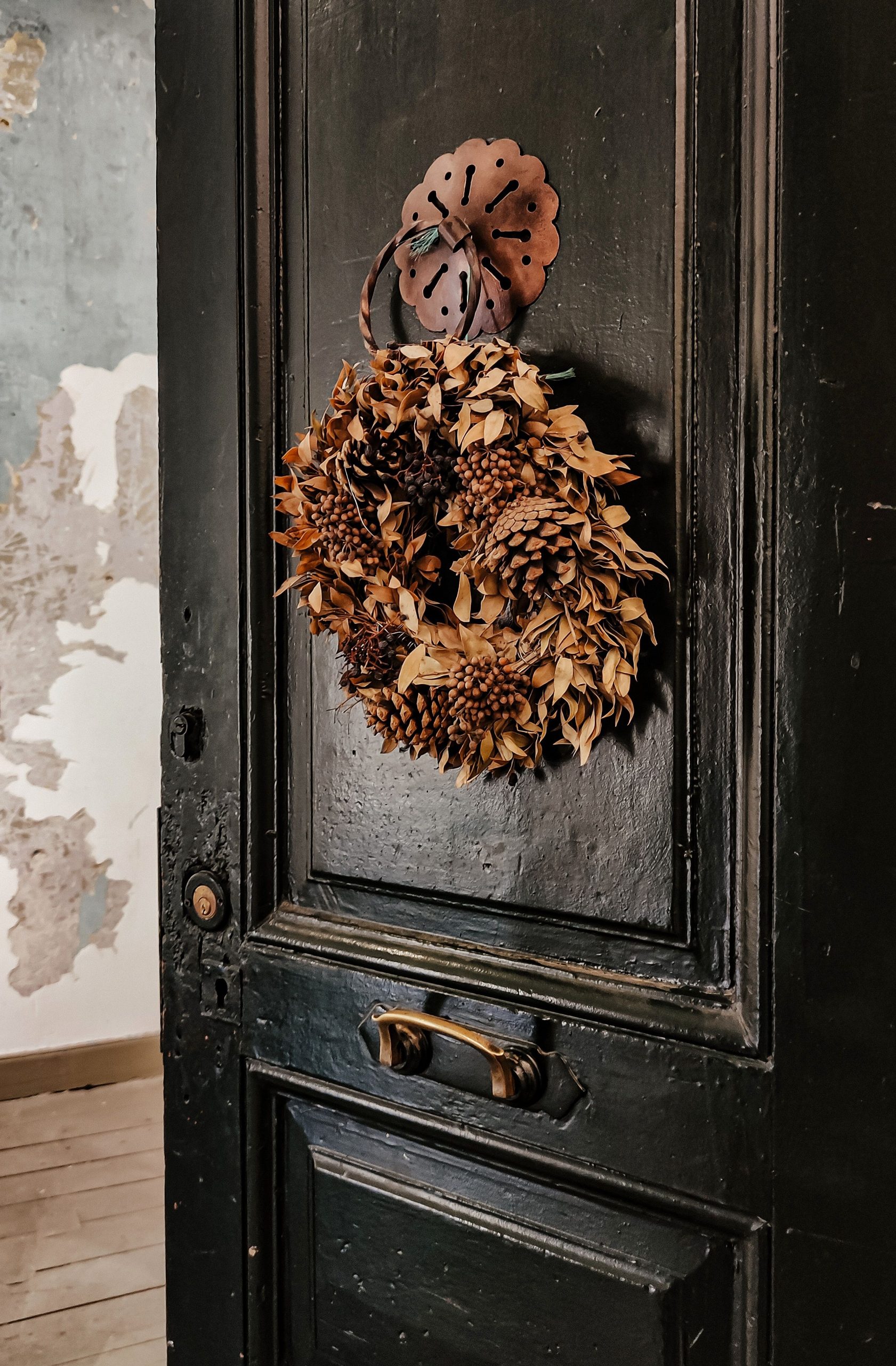 Charming rustic wooden door adorned with an ornamental pine cone wreath, perfect for seasonal decor.