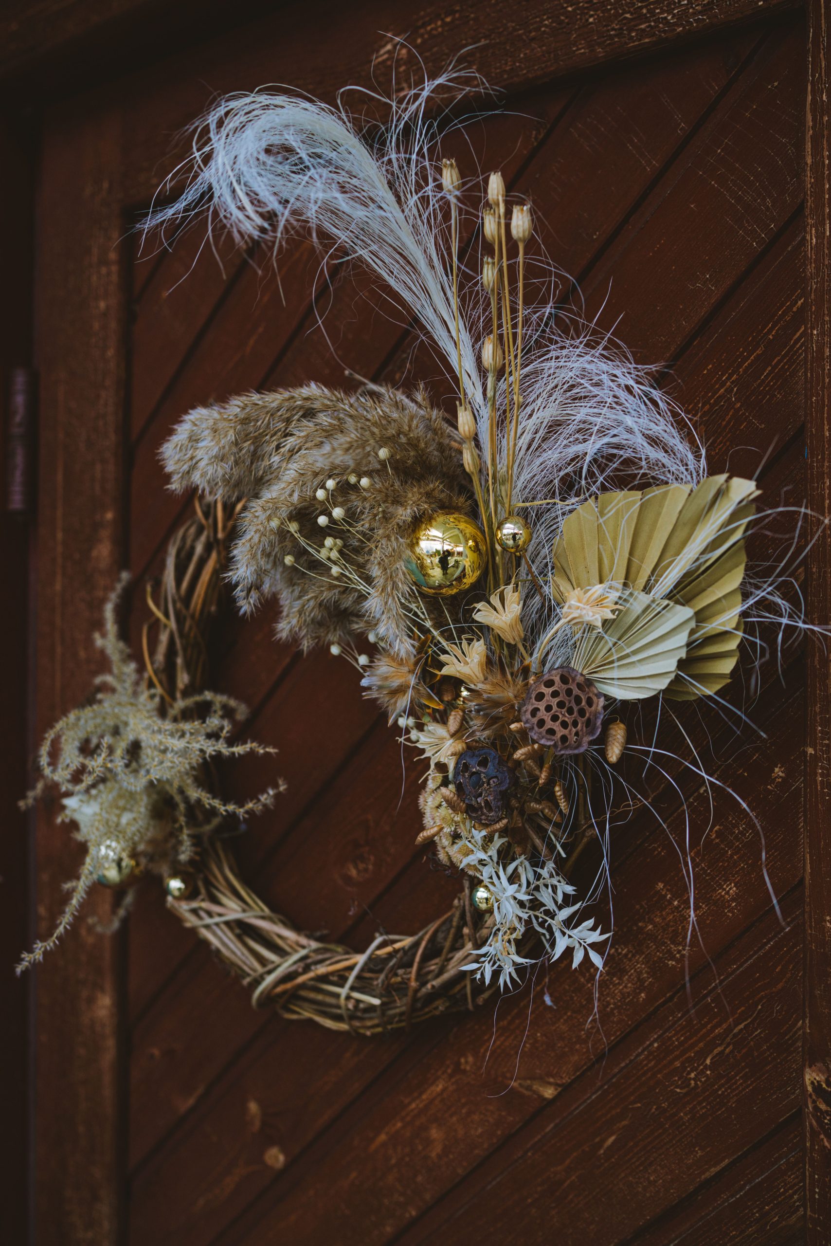 Close-up of a rustic wreath made with dried flowers and natural elements against a wooden door.