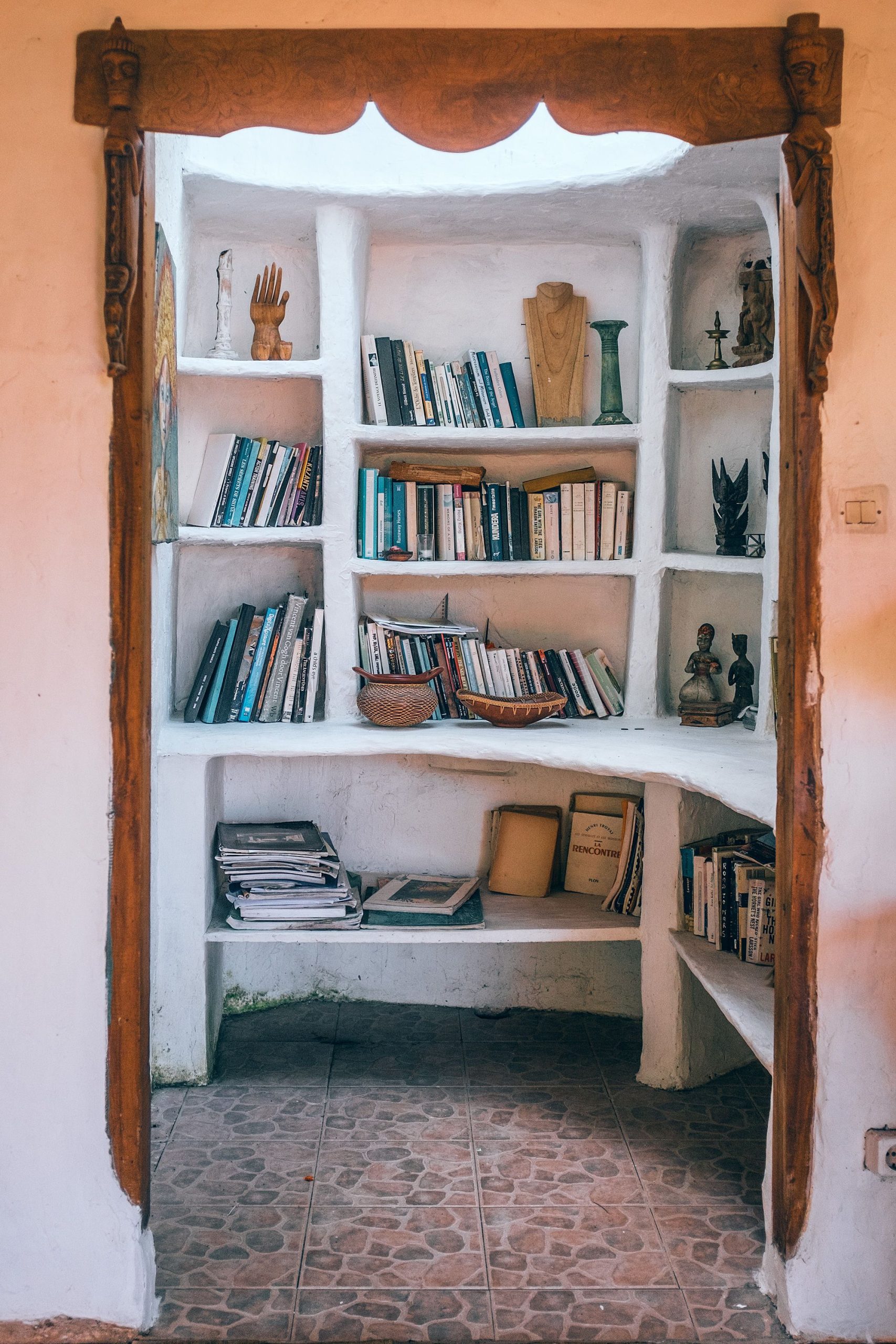 Collection of various books and decorative vases with small figures of human placed on white shelves in house