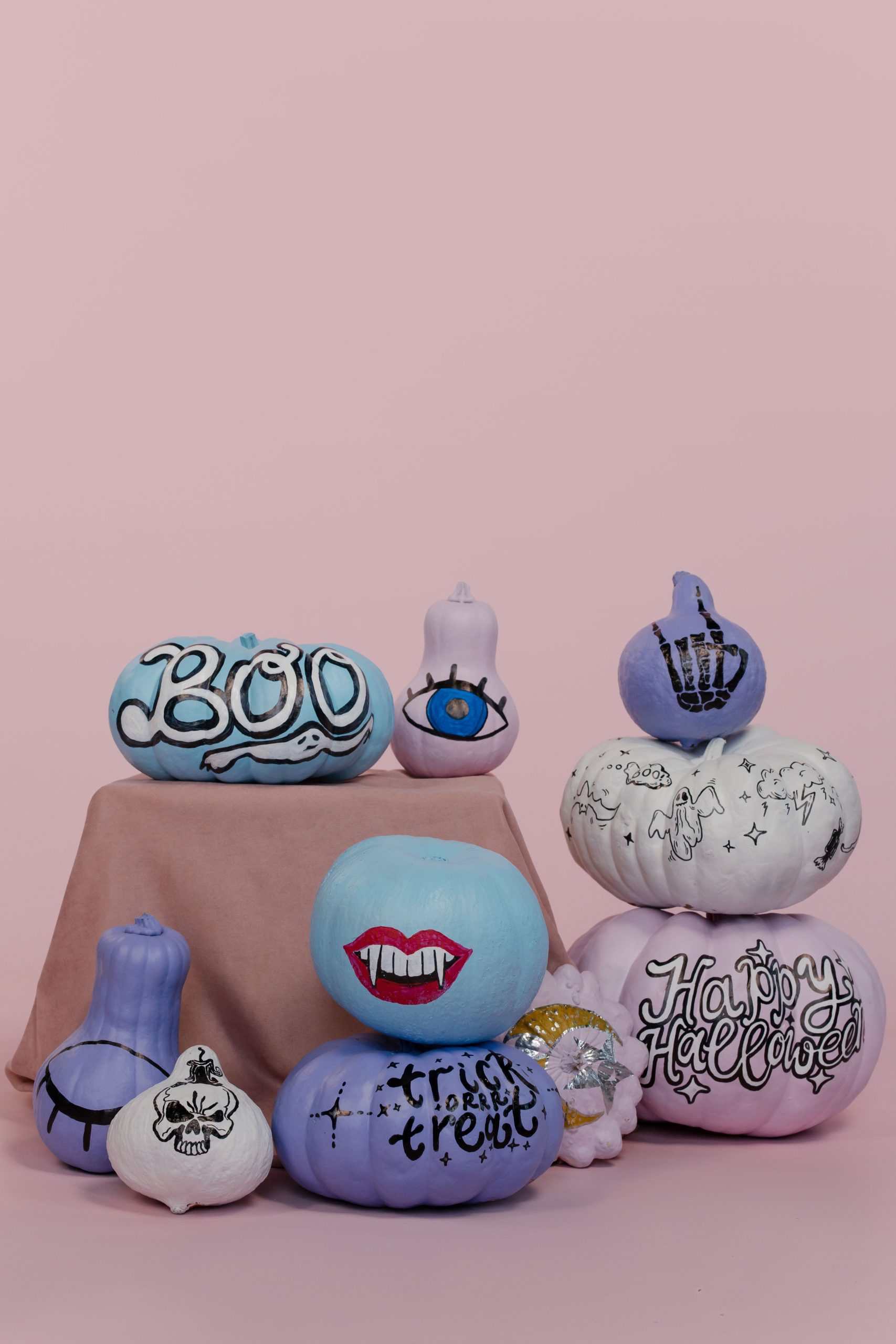 Colorful painted pumpkins with Halloween themes against a pink backdrop.