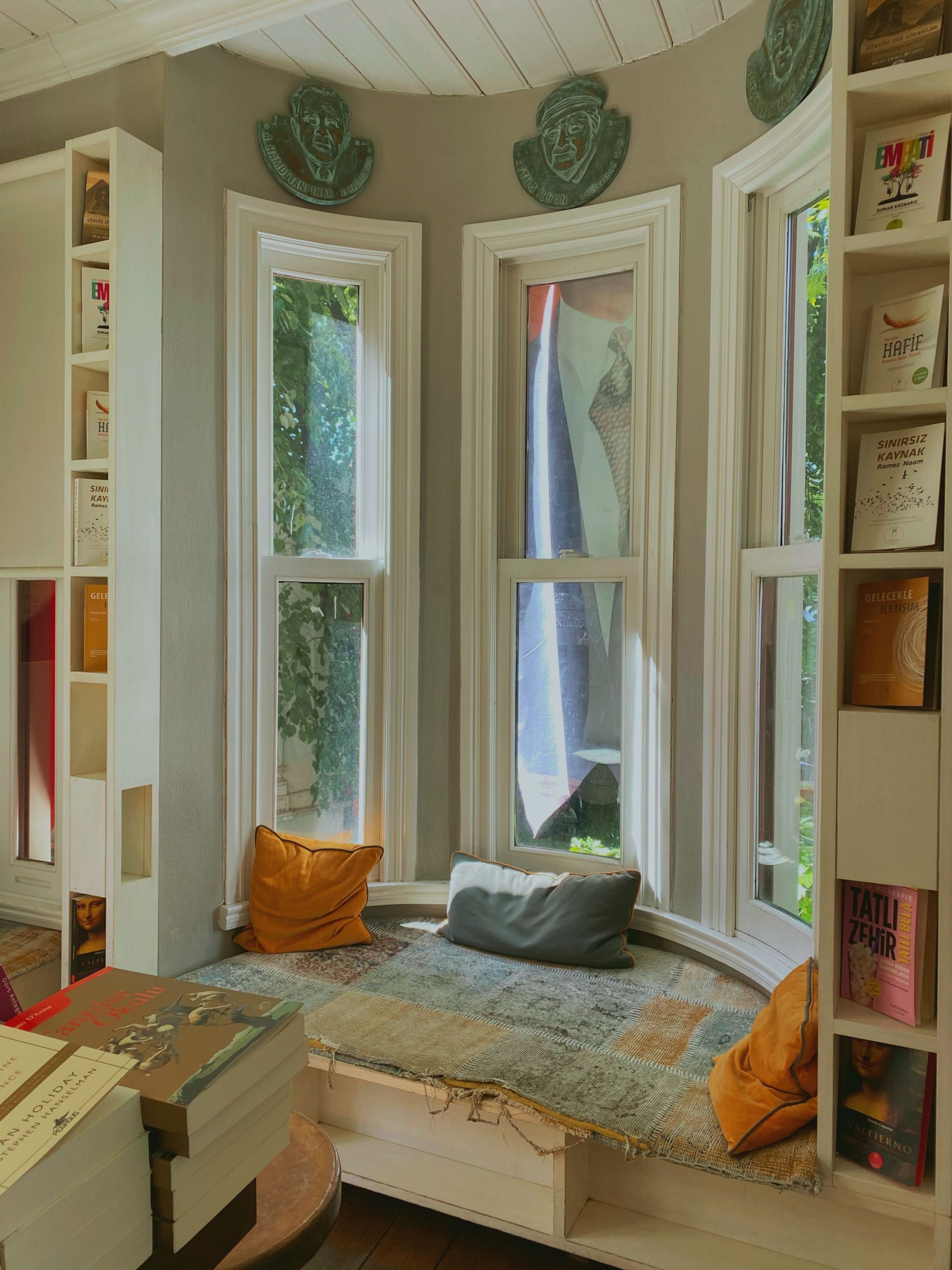 Comfortable reading nook with cushions and books surrounded by tall windows and bookshelves.